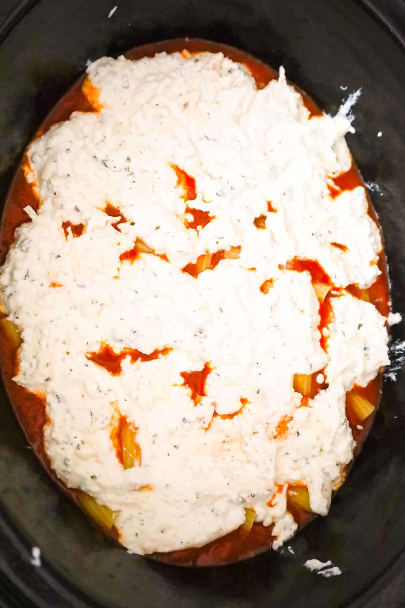 ricotta and sour cream mixture on top of marinara sauce in a crock pot