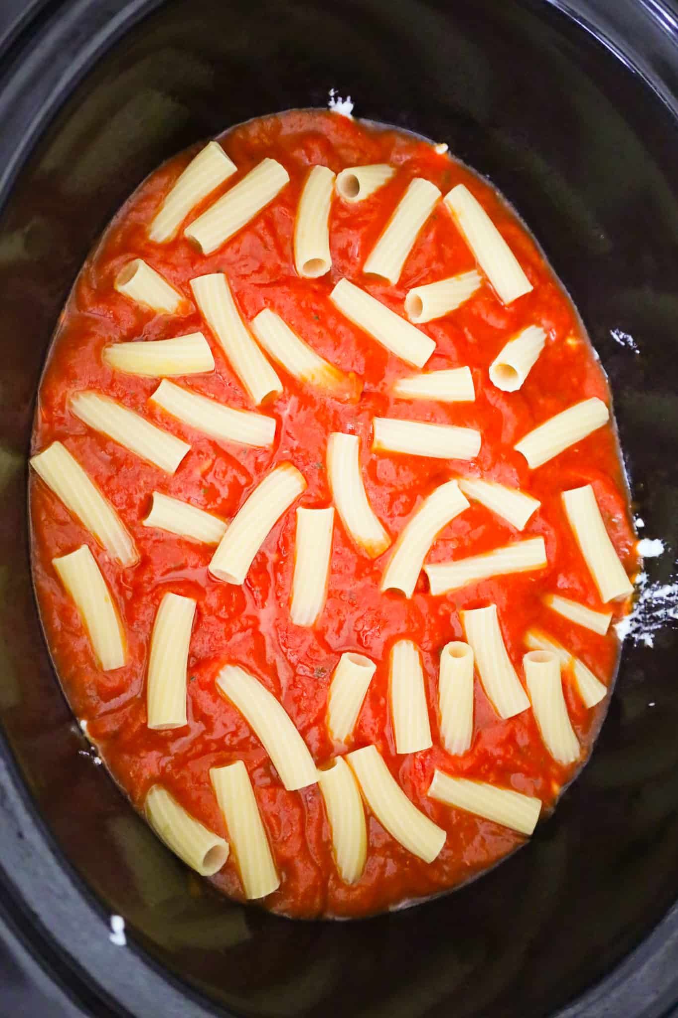 uncooked noodles on top of marinara sauce in a crock pot