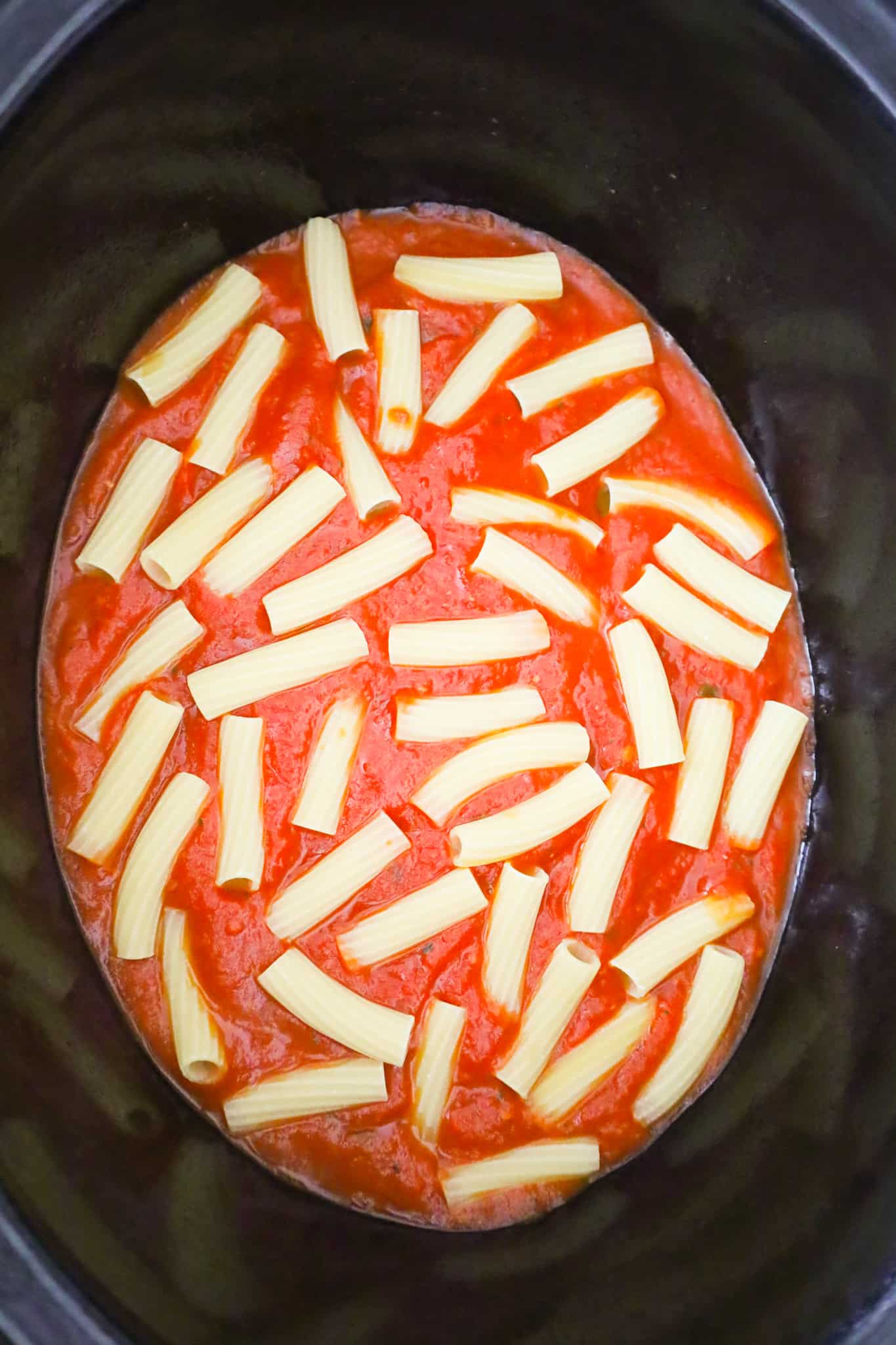 uncooked ziti noodles on top of marinara sauce in a slow cooker