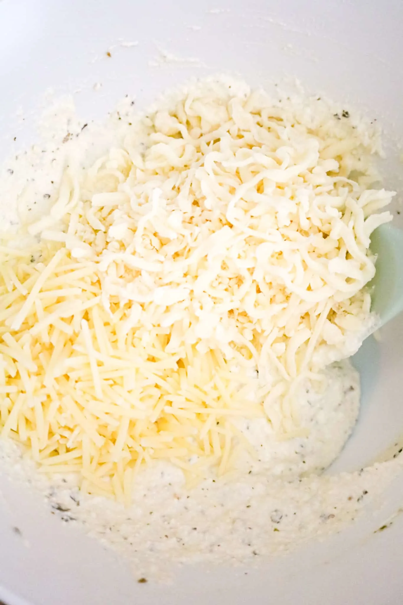 shredded mozzarella and parmesan on top of ricotta mixture in a mixing bowl