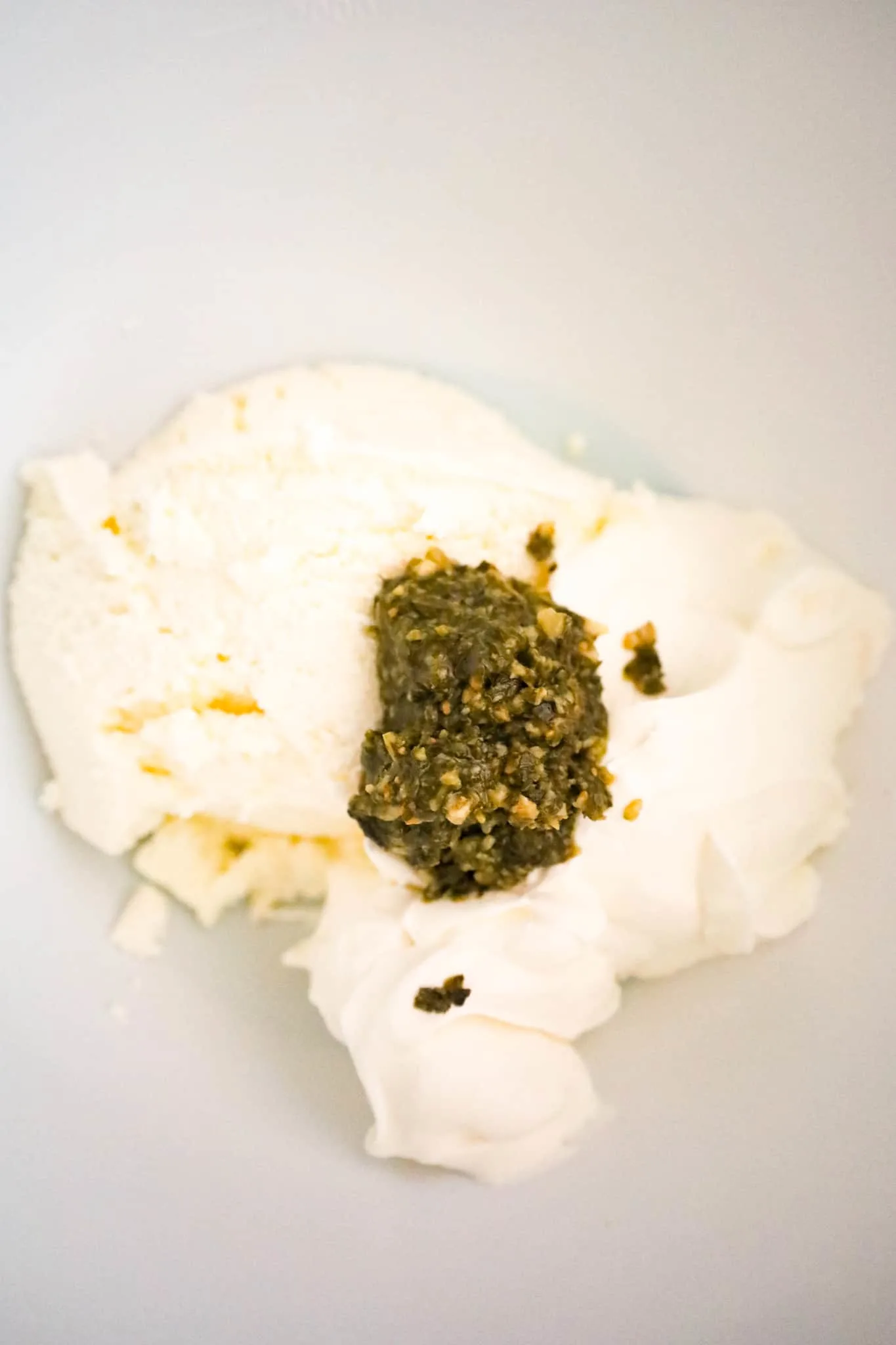 basil pesto on top of ricotta cheese and sour cream in a mixing bowl
