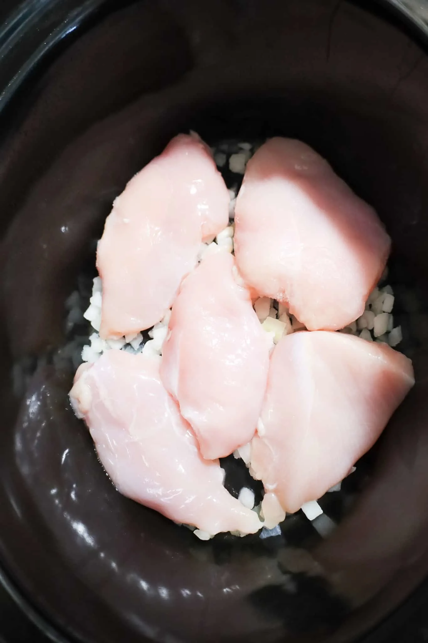 boneless, skinless chicken breasts on top of diced onions in a crock pot