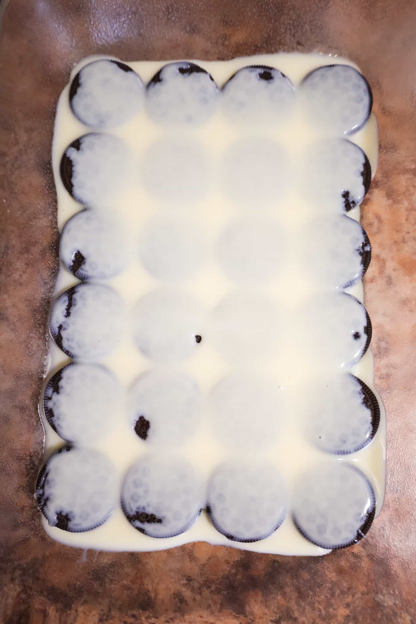 sweetened condensed milk poured over Oreo cookies in a baking dish