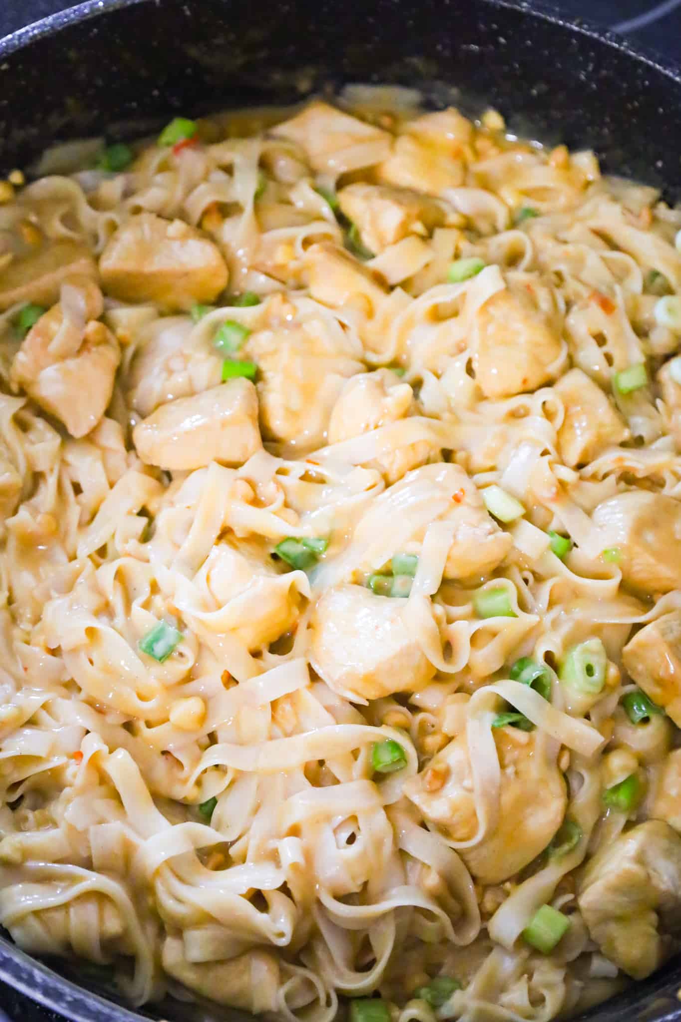 rice noodles and chicken breast chunks tossed in peanut sauce in a saute pan