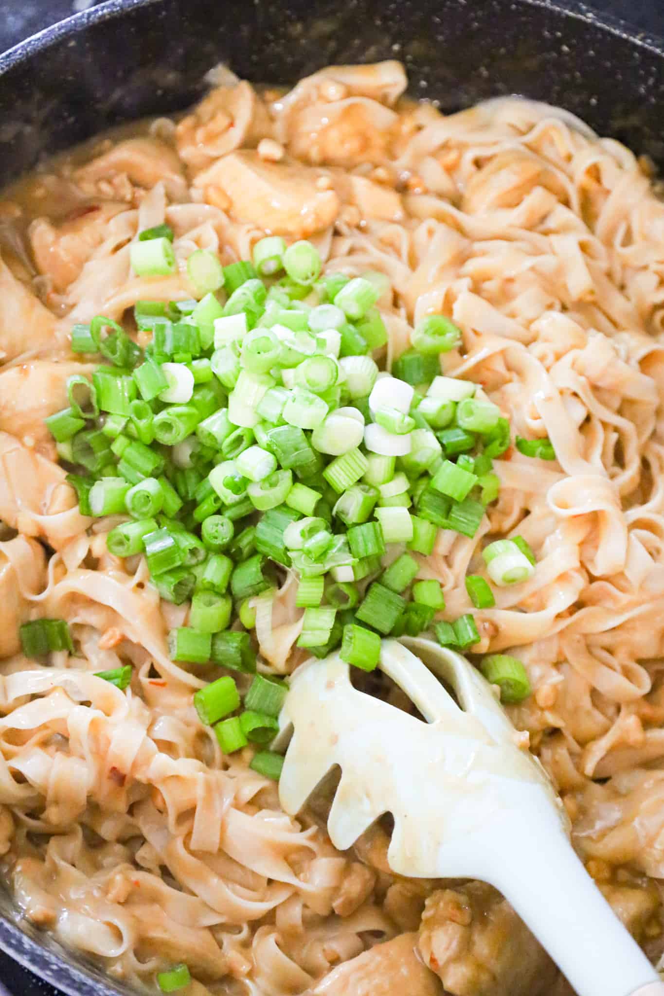 chopped green onions on top of chicken and rice noodles in a saute pan