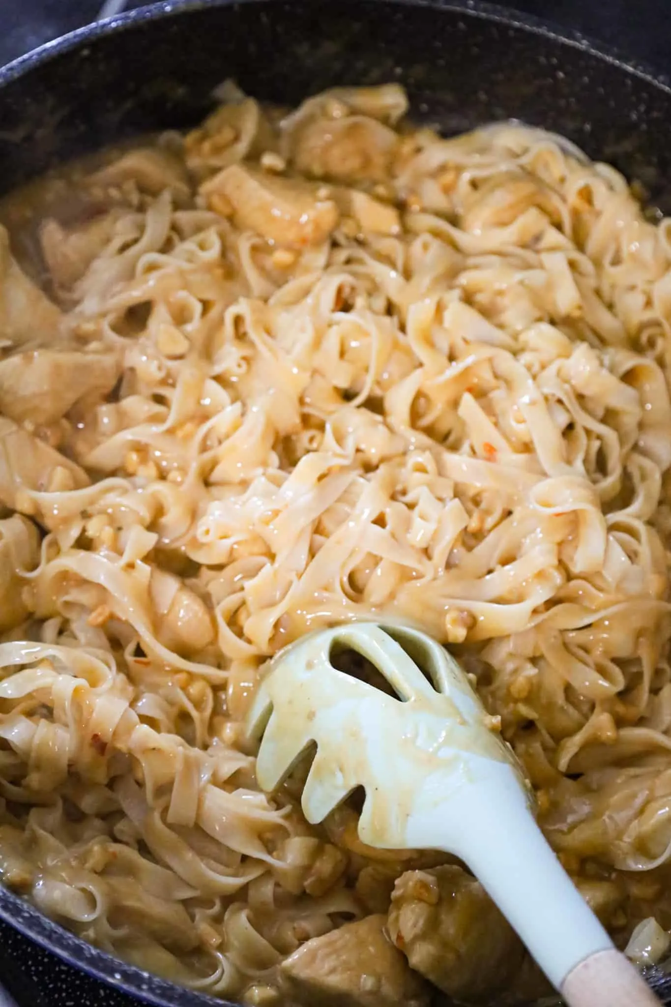 chicken breast chunks and rice stick noodles being stirred in peanut butter sauce