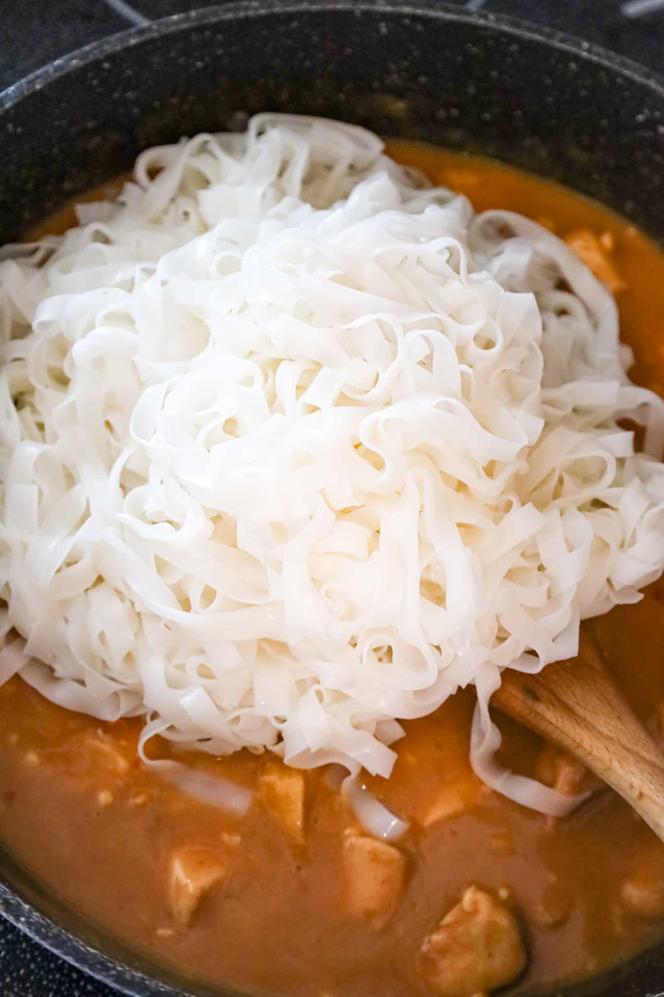 cooked rice noodles on top of peanut butter chicken mixture in a saute pan