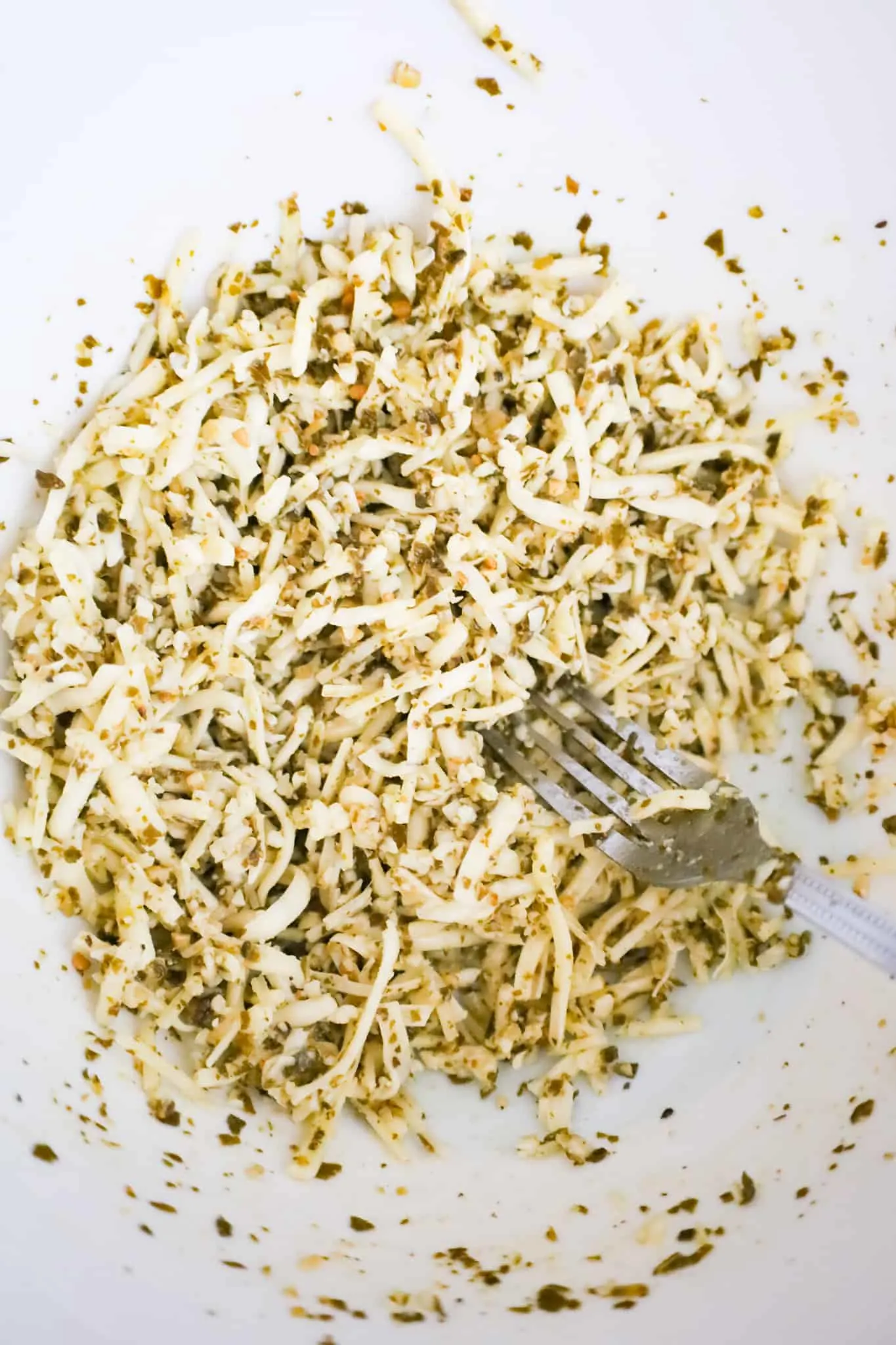 mixture of basil pesto, shredded mozzarella and shredded parmesan in a mixing bowl