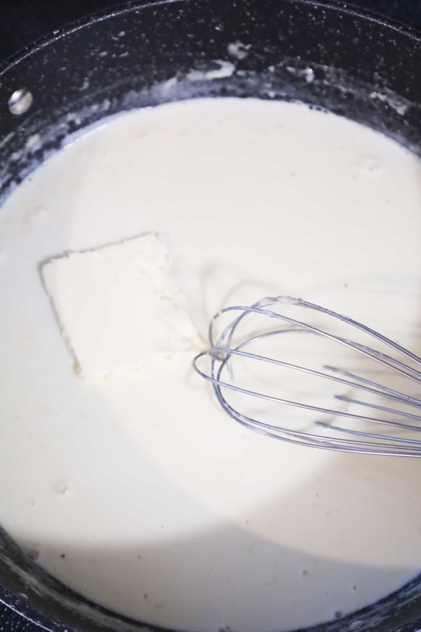 butter added to creamy alfredo sauce in a pan
