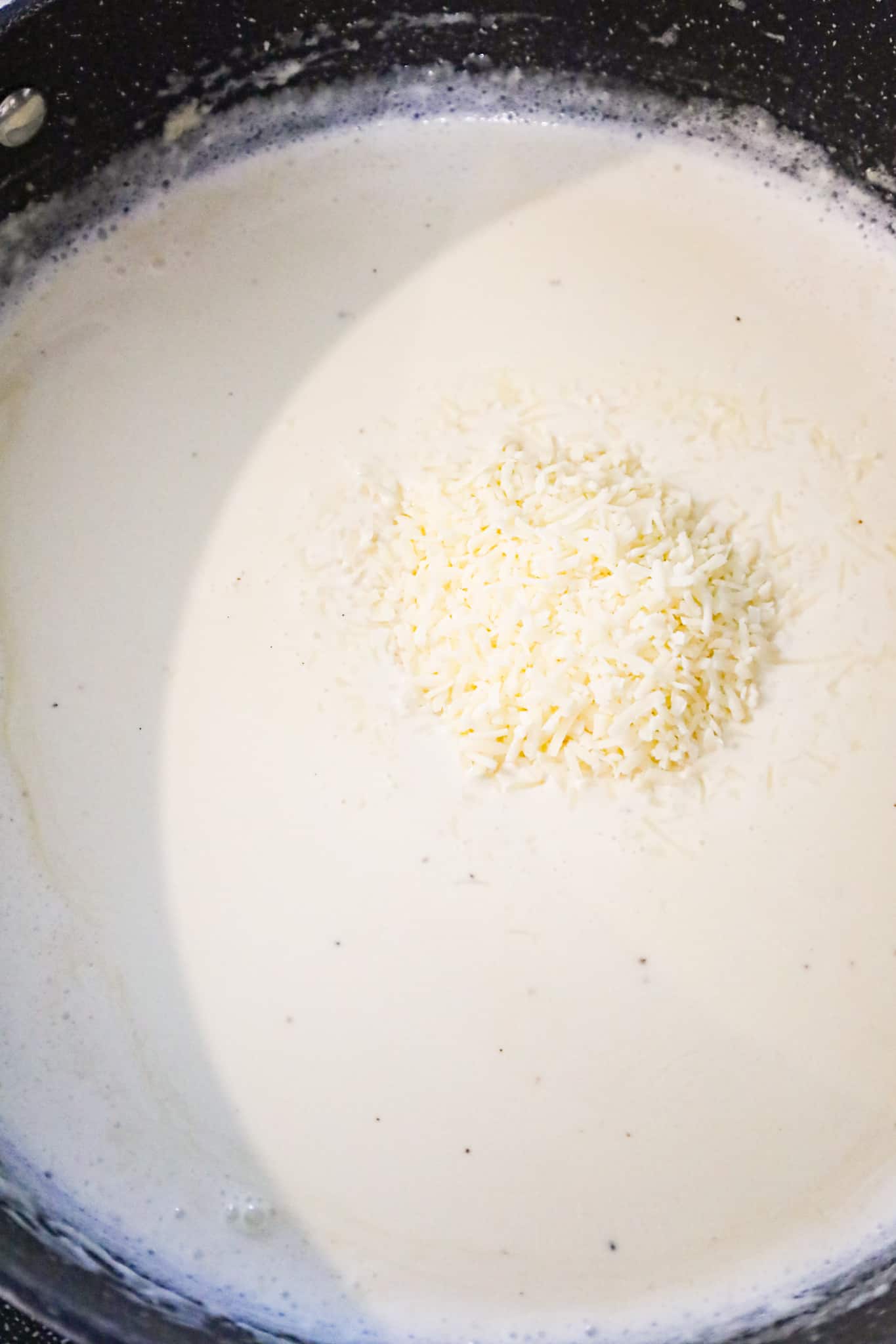 shredded parmesan cheese added to cream sauce in a pan