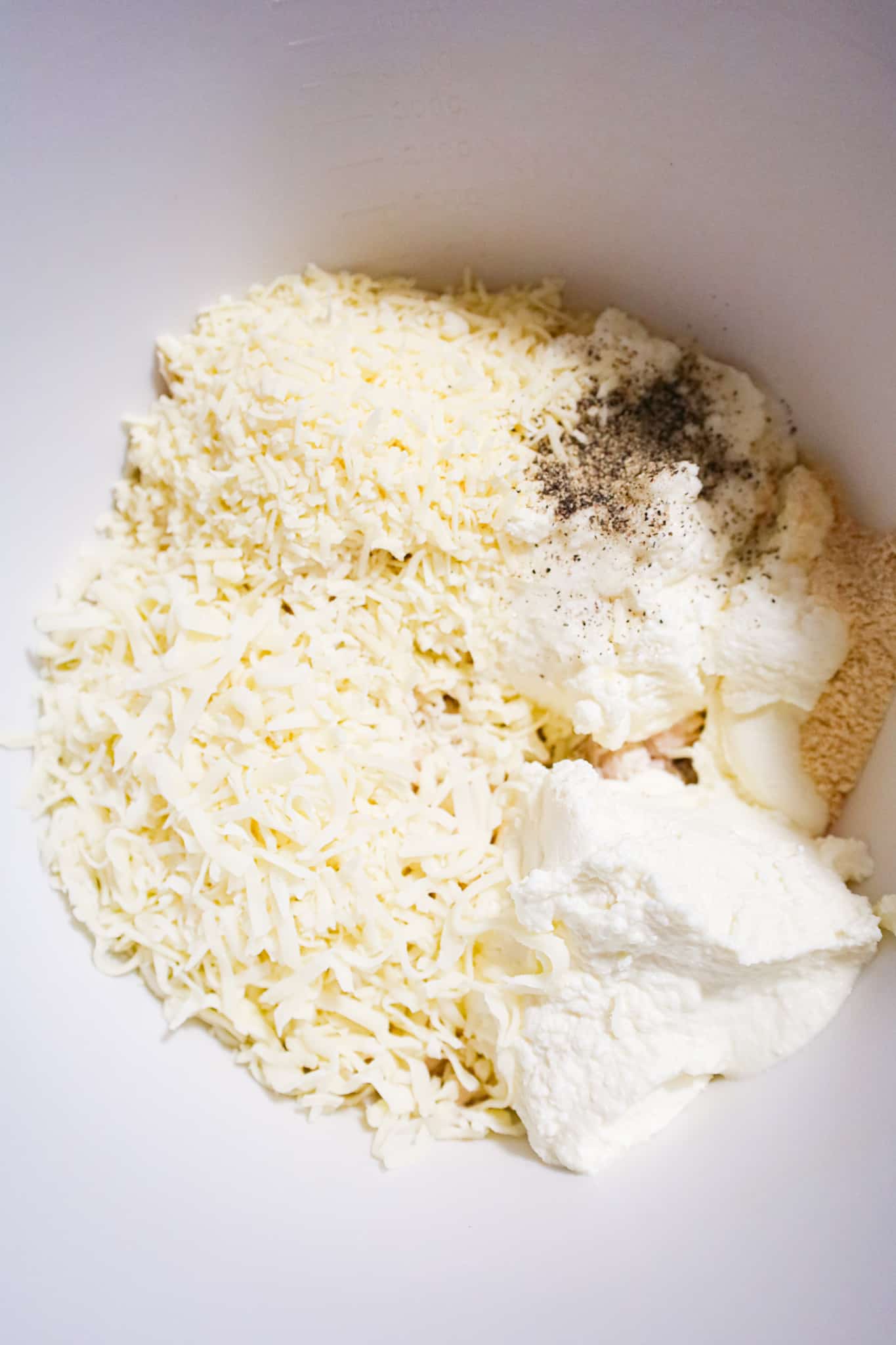 ricotta, shredded mozzarella, shredded parmesan and spices on top of shredded chicken in a mixing bowl
