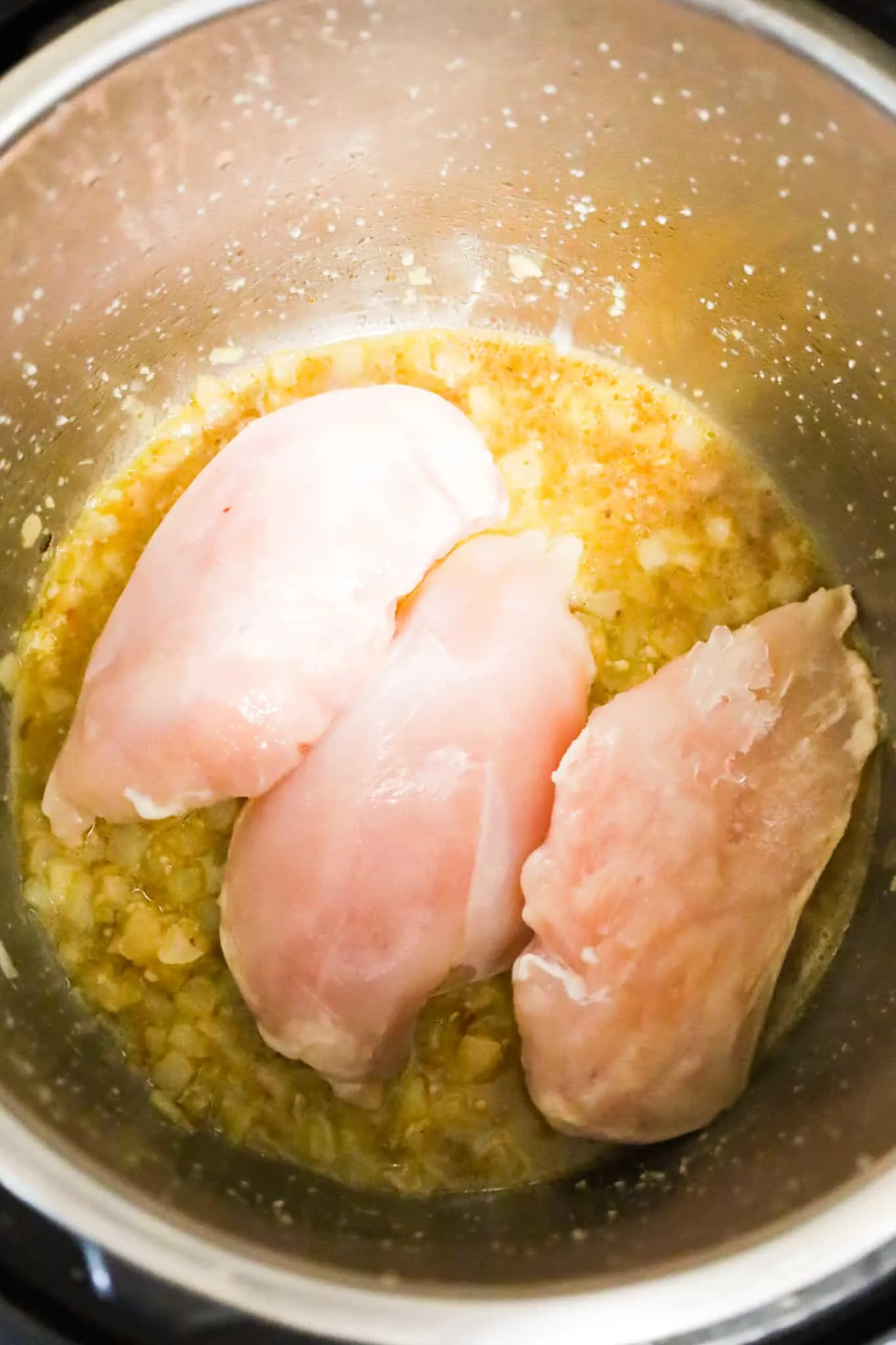 raw chicken breasts on top of chicken broth and cooked diced onions in an Instant Pot