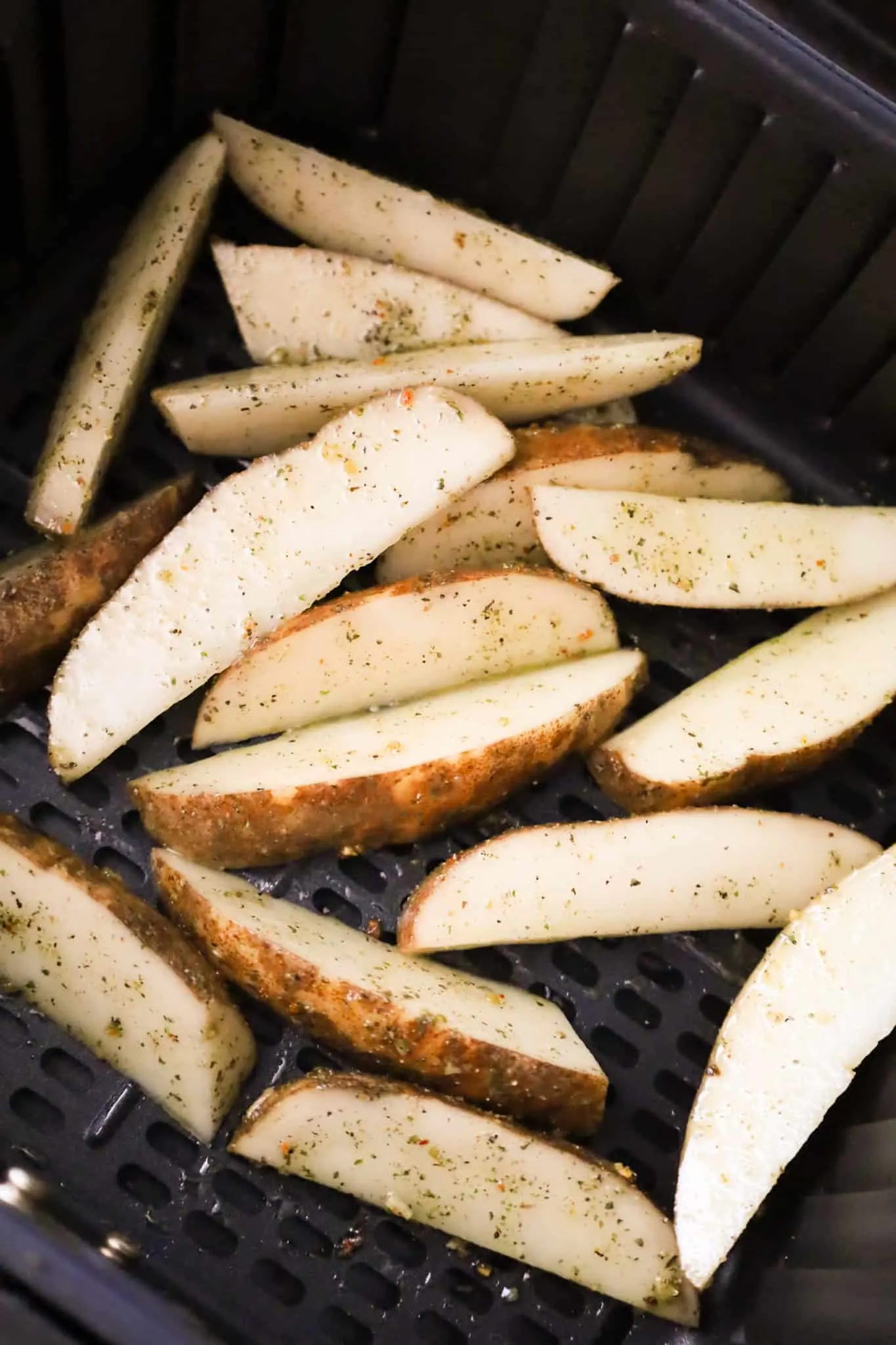 potato wedges in an air fryer basket before cooking
