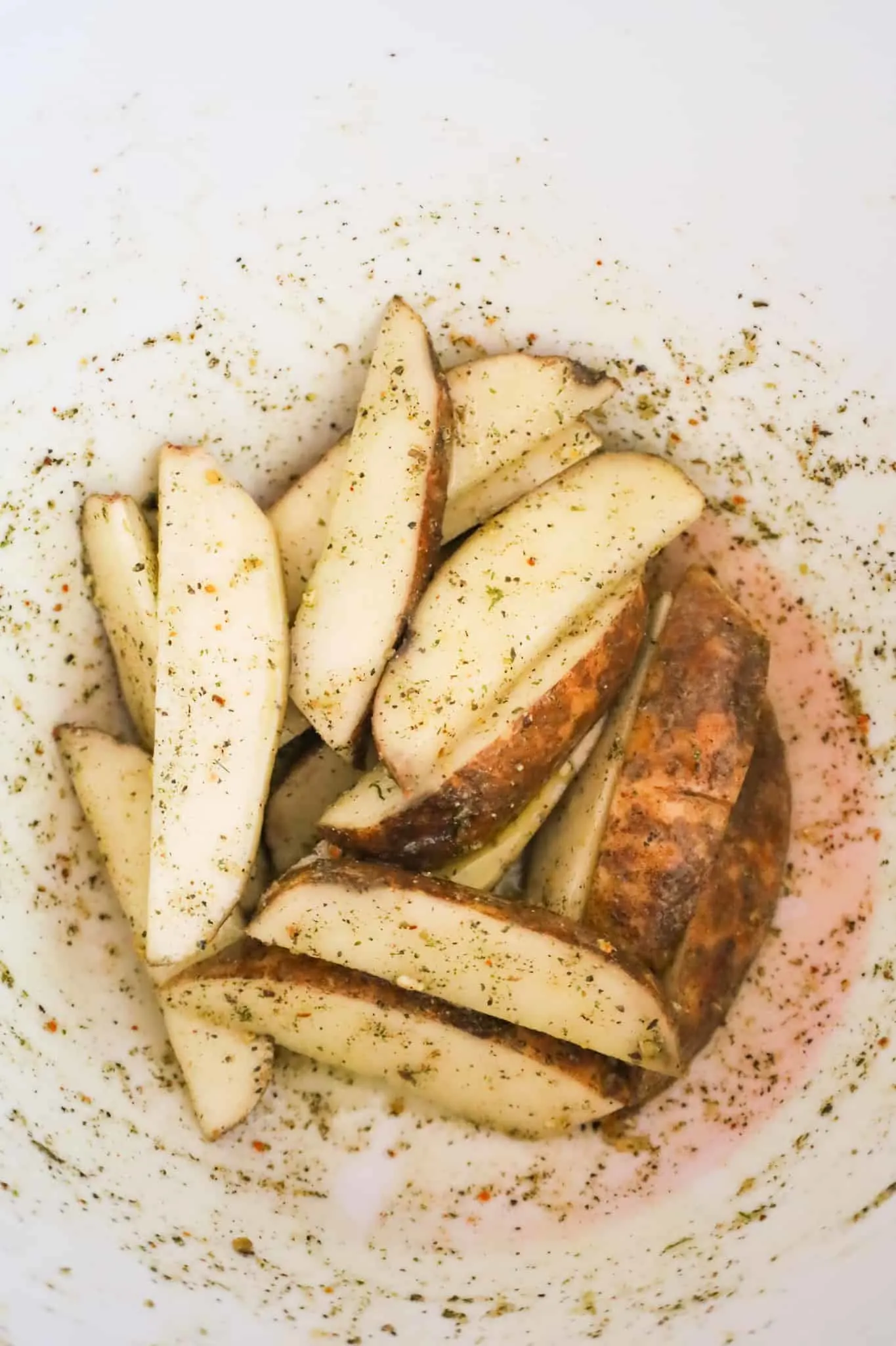 raw potato wedges tossed in olive oil and seasoning in a mixing bowl