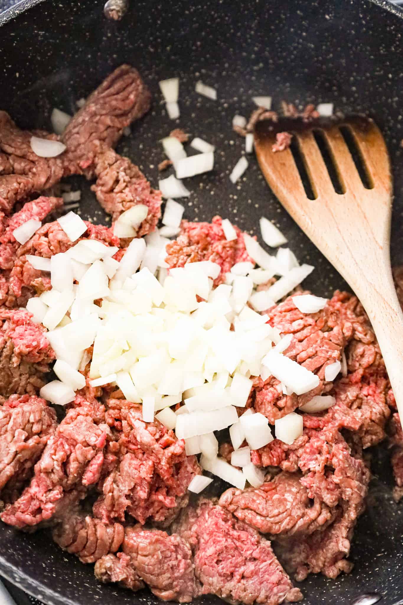 diced onions on top of raw ground beef in a saute pan