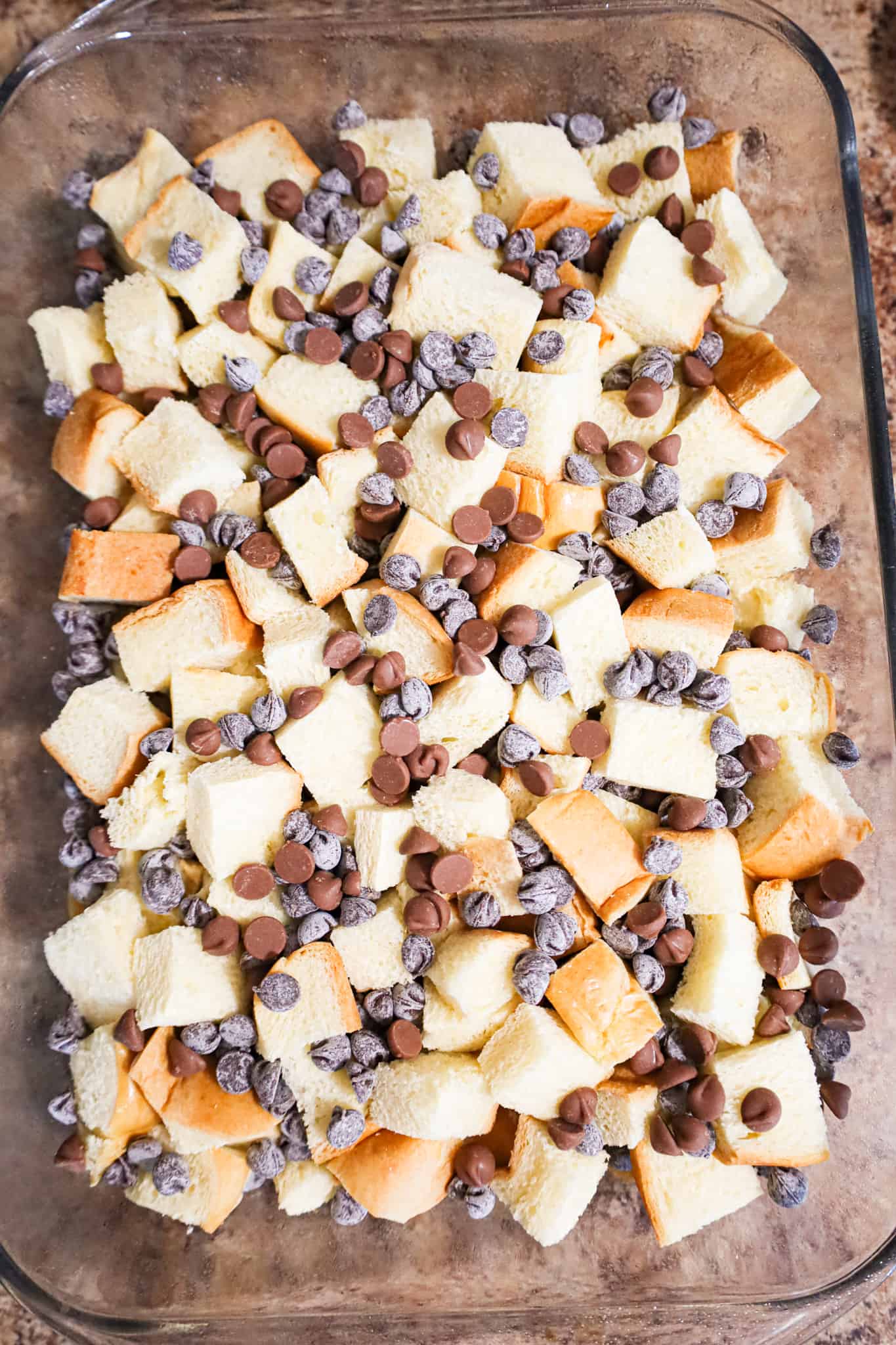 chocolate chips on top of cubed brioche bread in a baking dish