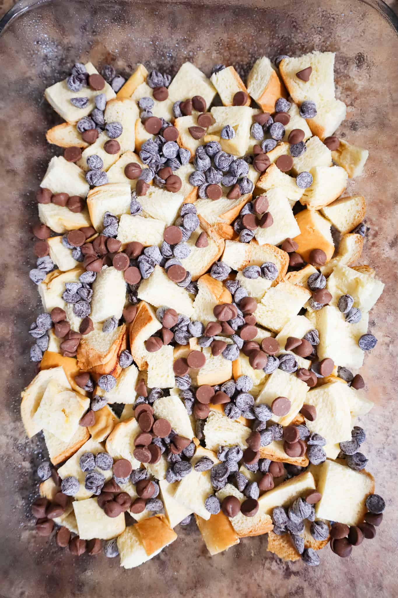 chocolate chips on top of cubed brioche bread in the bottom of a baking dish