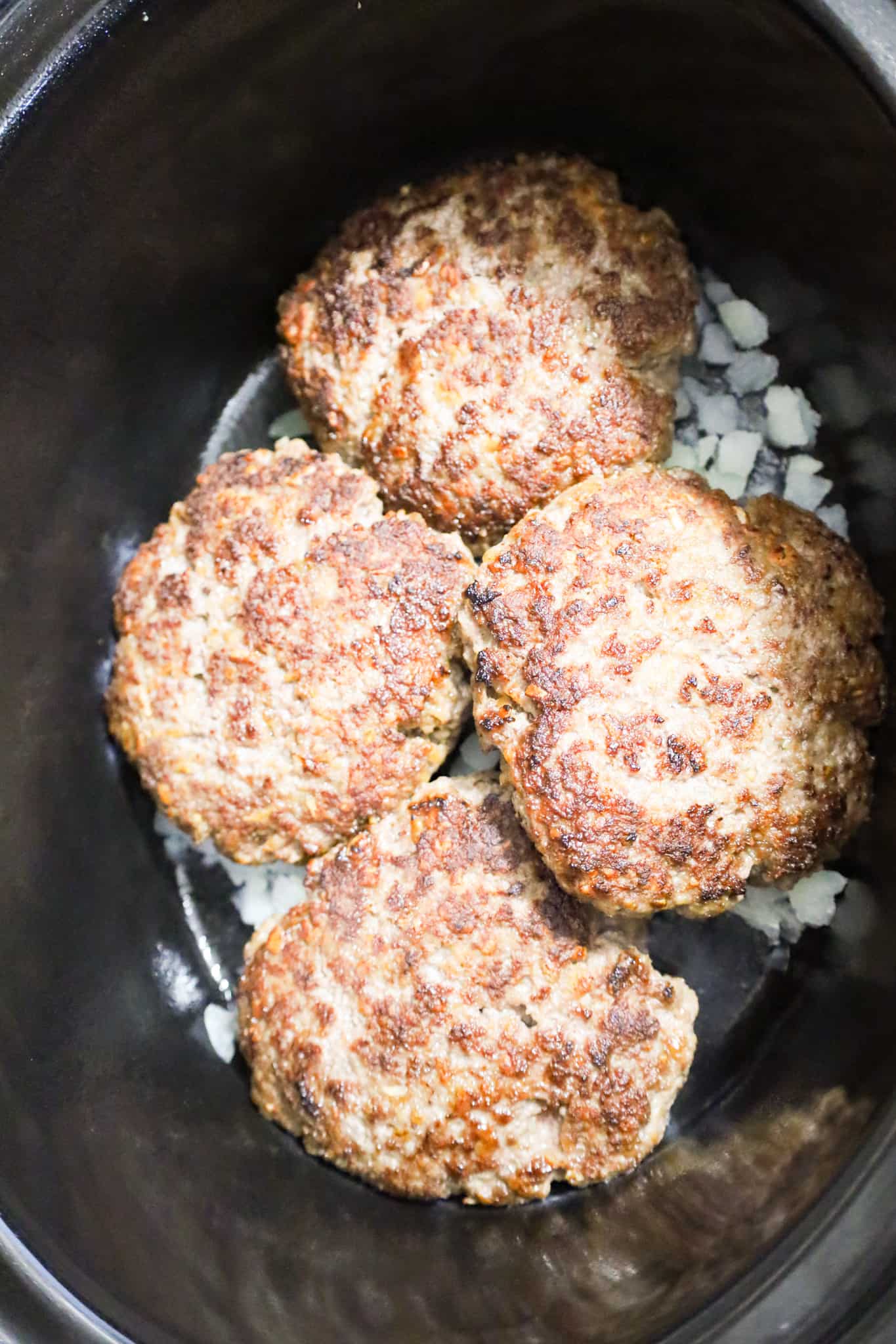 browned hamburger patties on top of diced onions in a crock pot