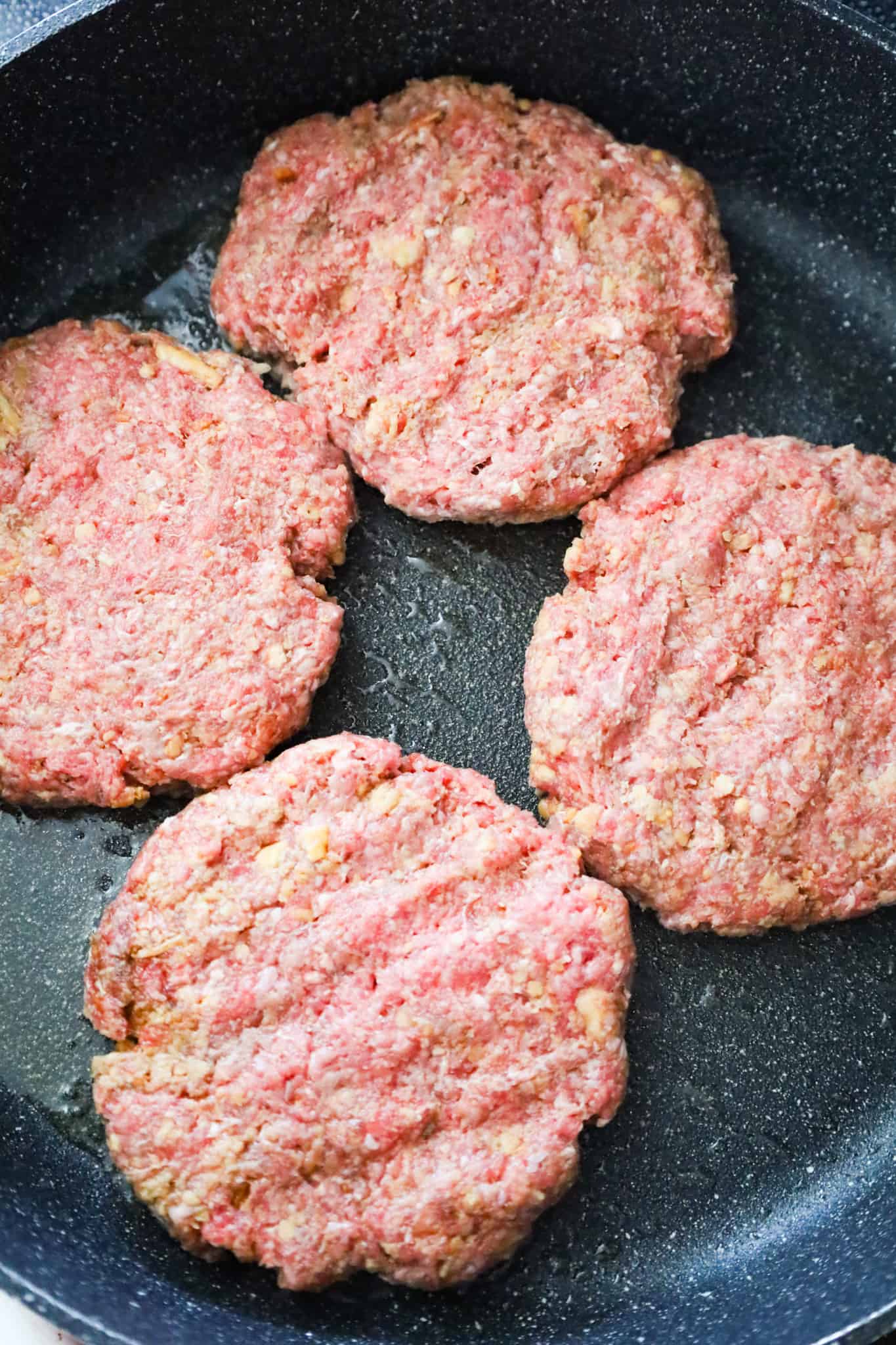raw ground beef patties in a saute pan