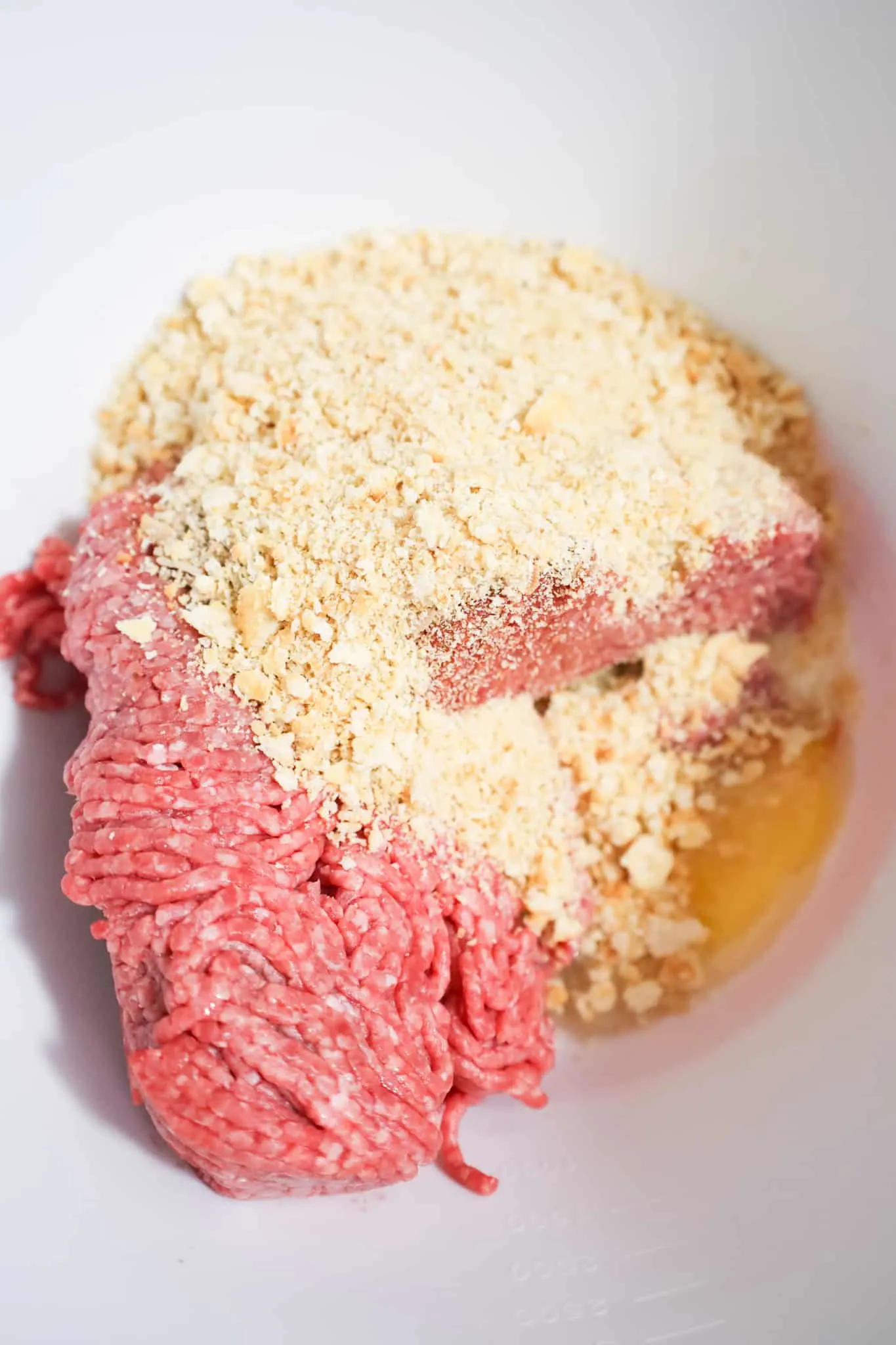 ritz cracker crumbs on top of ground beef in a mixing bowl