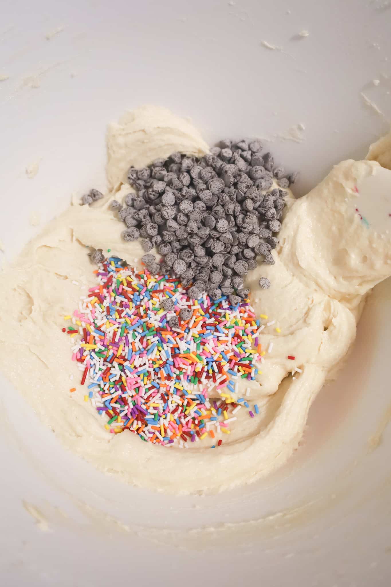 colourful sprinkles and mini chocolate chips on top of sugar cookie dough in a mixing bowl