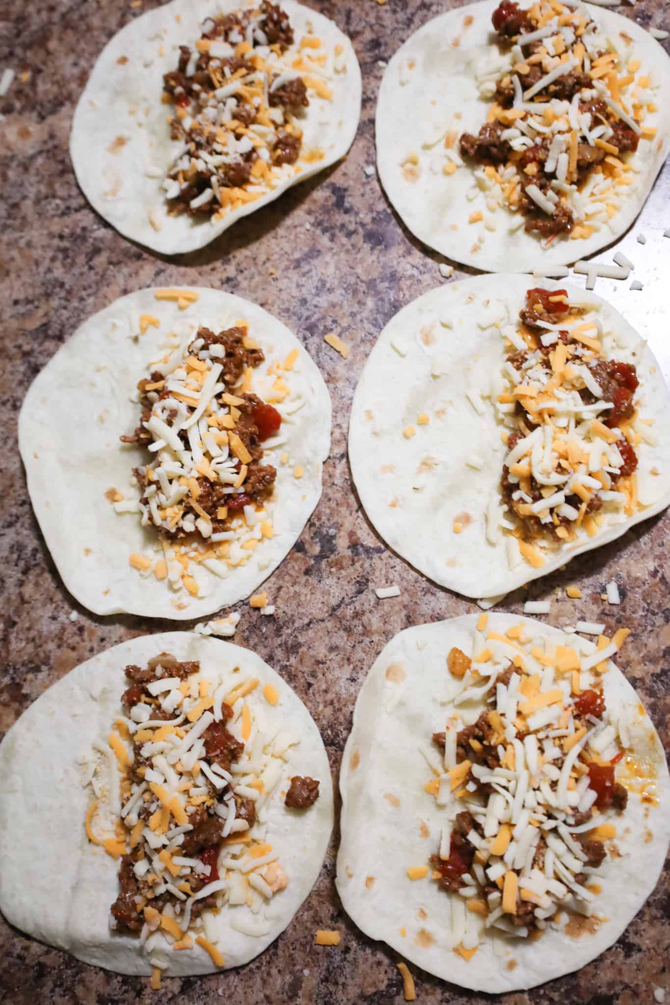 shredded cheese and beef taco meat on half of small flour tortillas