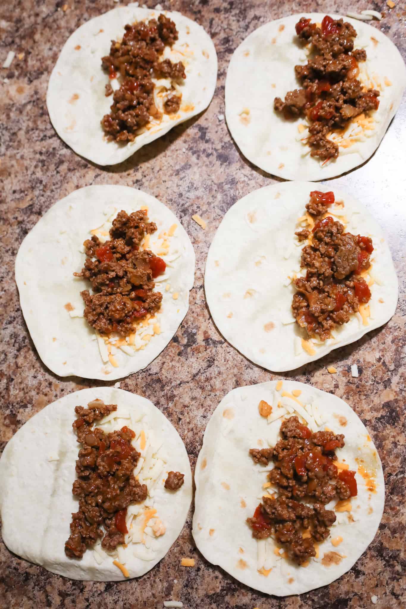 beef taco meat on top of shredded cheese on flour tortillas