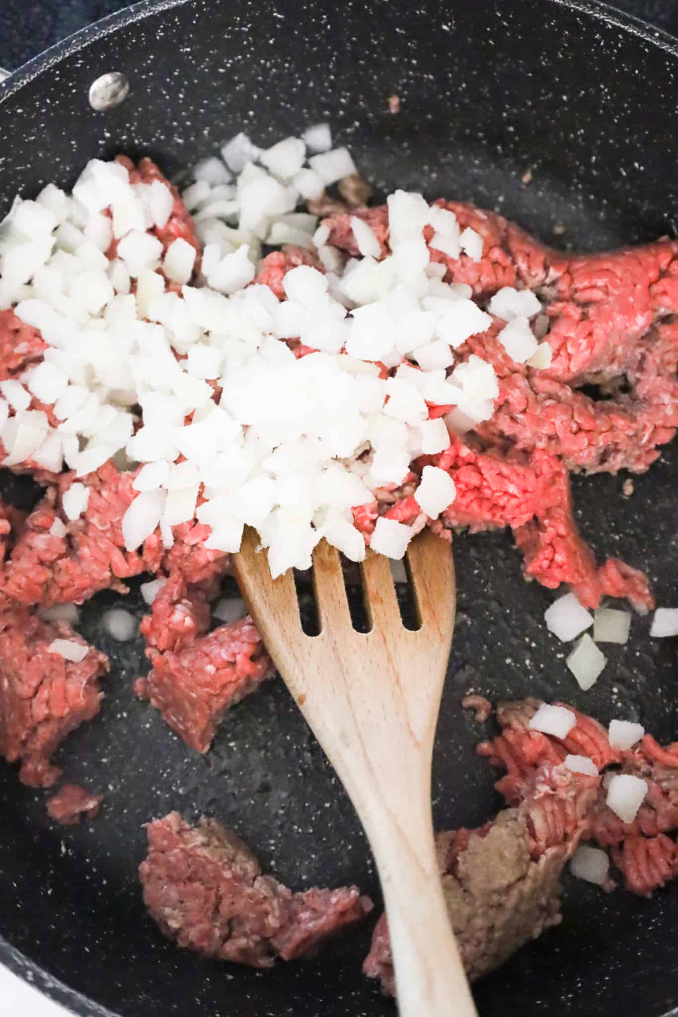 diced onions on top of raw ground beef in a saute pan