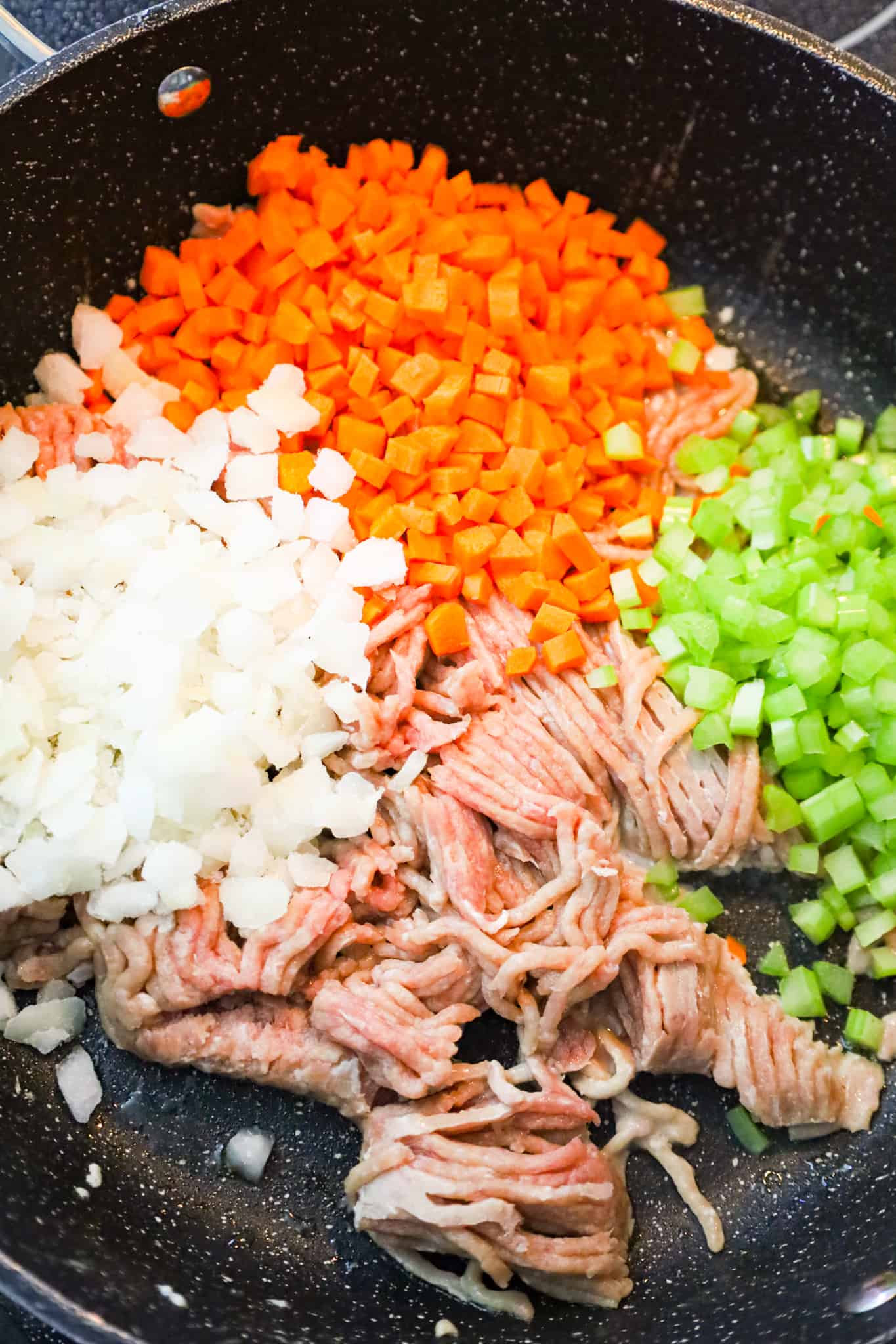 diced onions, diced carrots and diced celery on top of uncooked ground turkey in a skillet