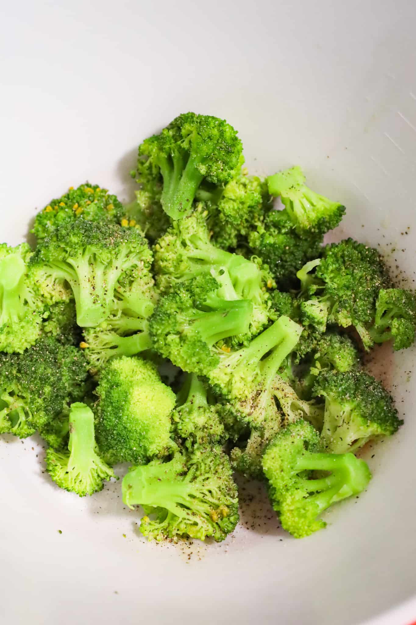 salt, pepper and olive oil on top of cooked broccoli in a bowl