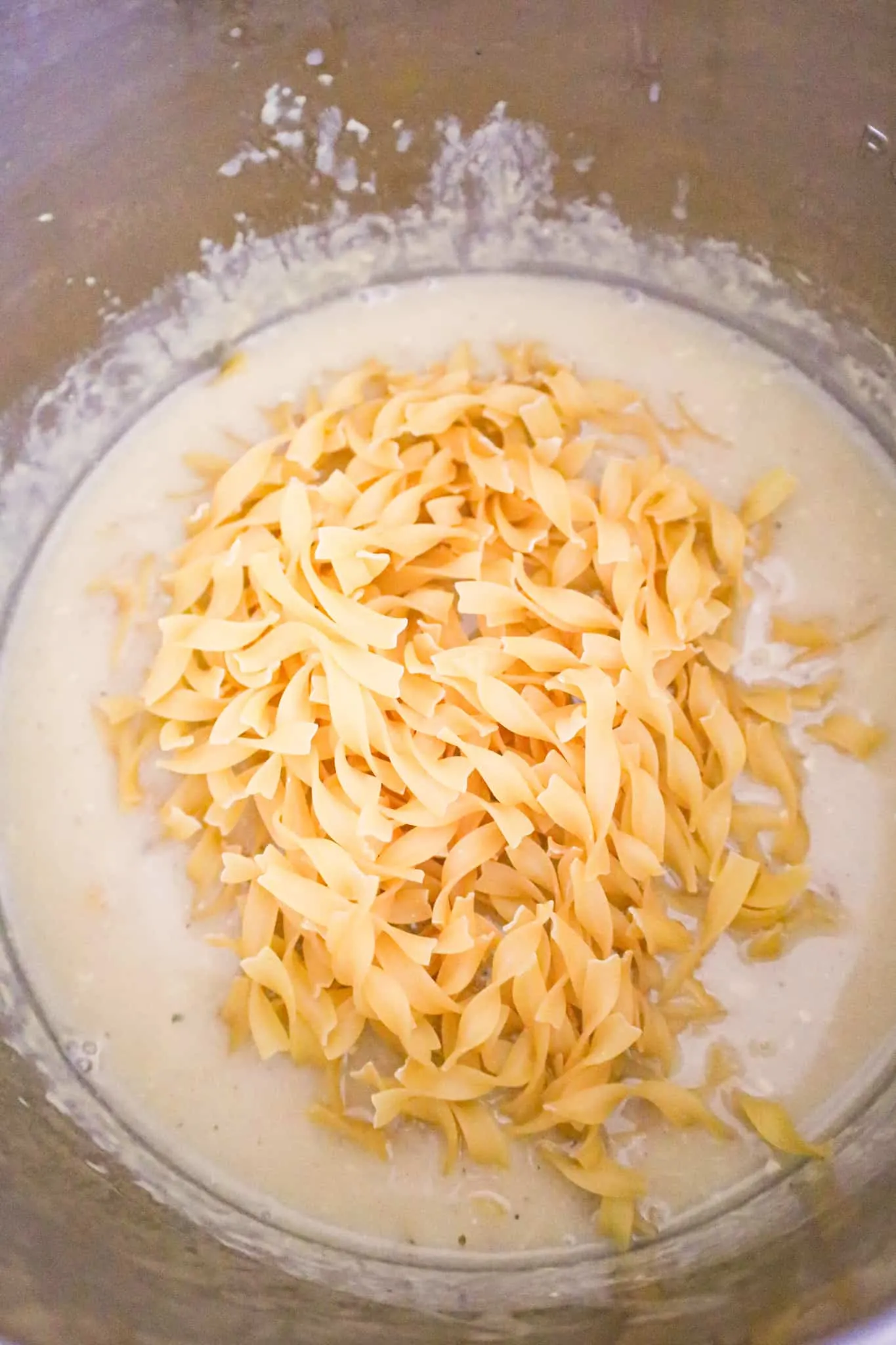 uncooked egg noodles added to Instant Pot with creamy gravy mixture