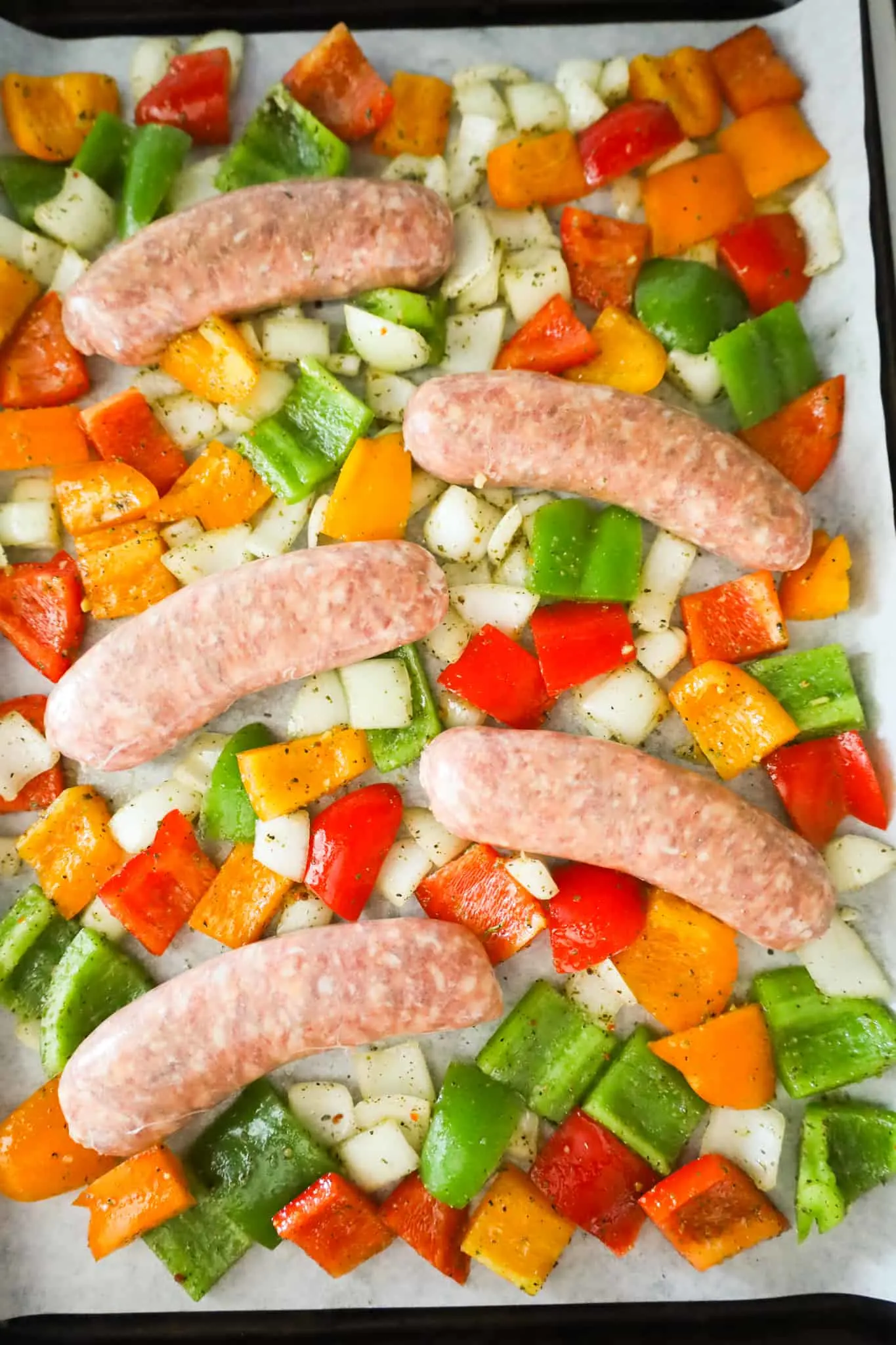 raw Italian sausage and peppers on a baking sheet