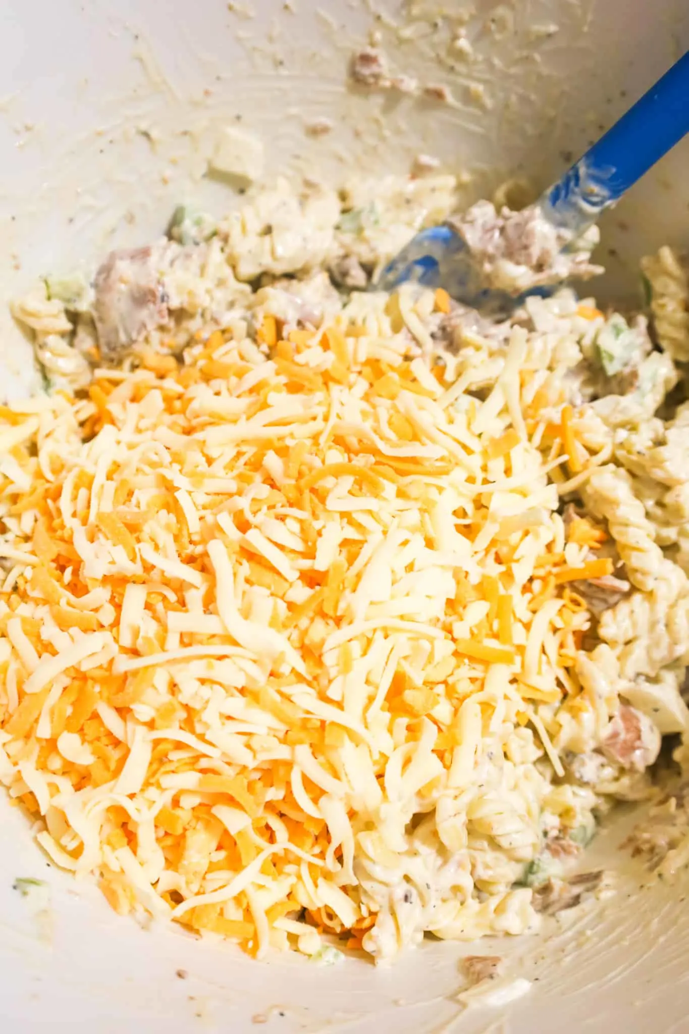shredded cheese on top of pasta salad in a mixing bowl