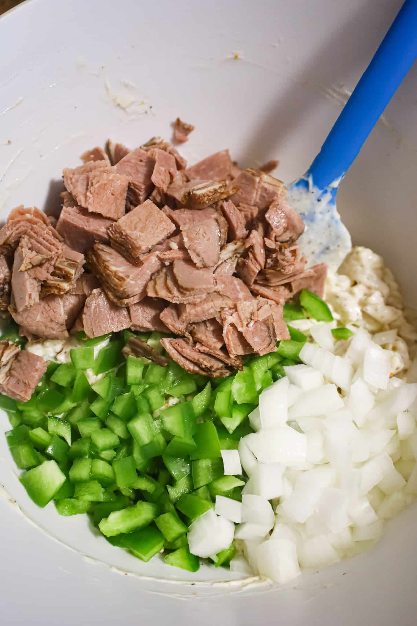 diced roast beef, green peppers and onion on top of noodles in a mixing bowl
