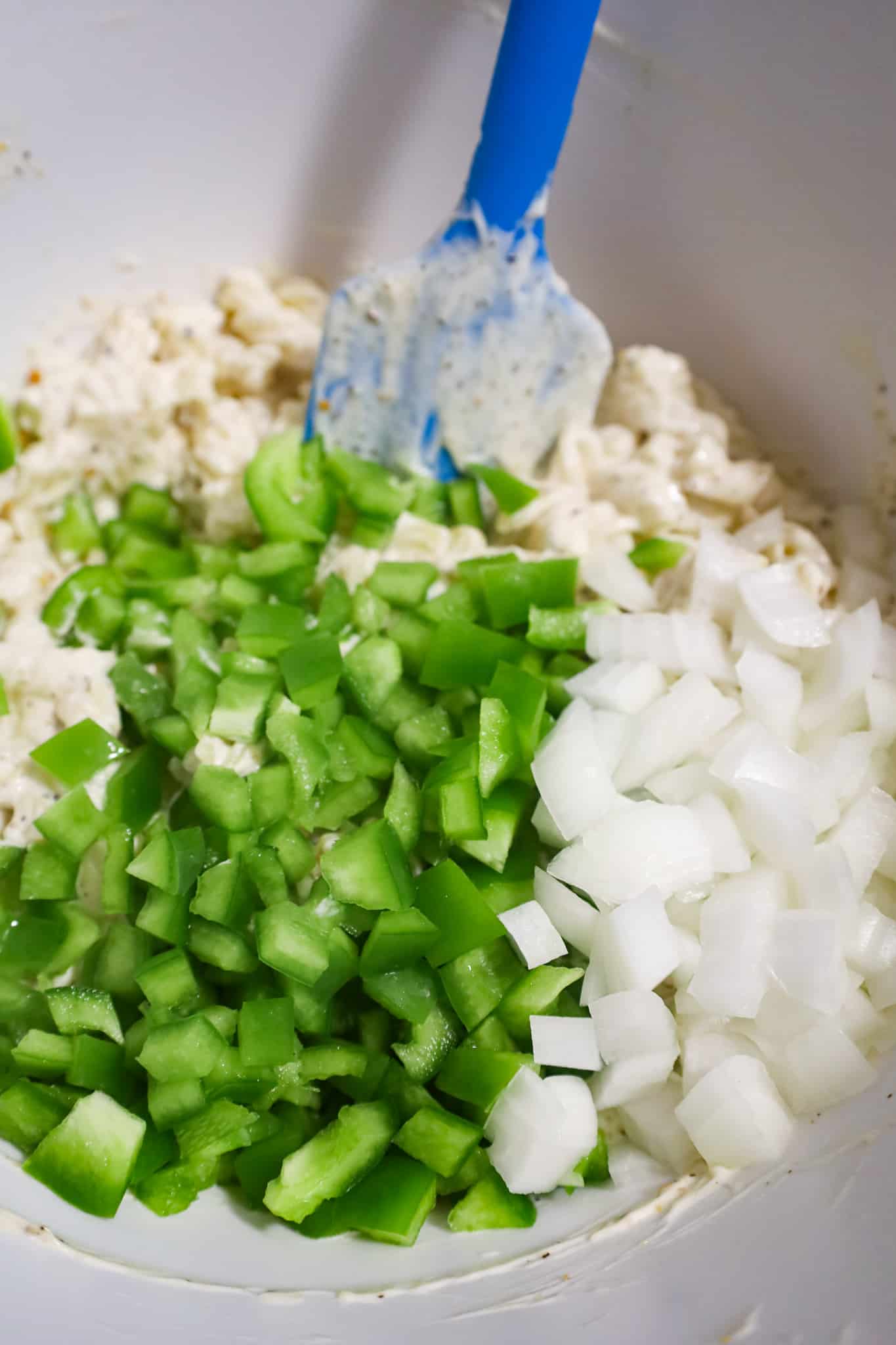 diced green peppers and onion on top of mayo coated noodles in a mixing bowl