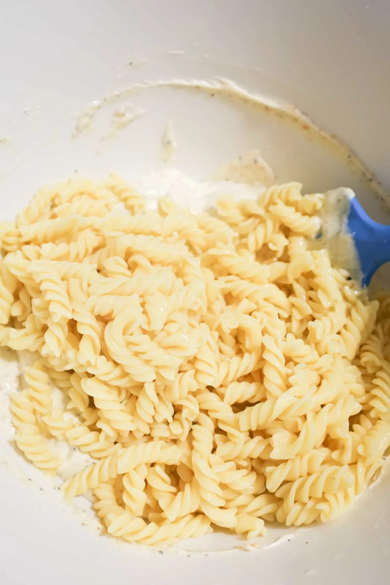 cooked fusilli noodles on top of mayo mixture in a mixing bowl