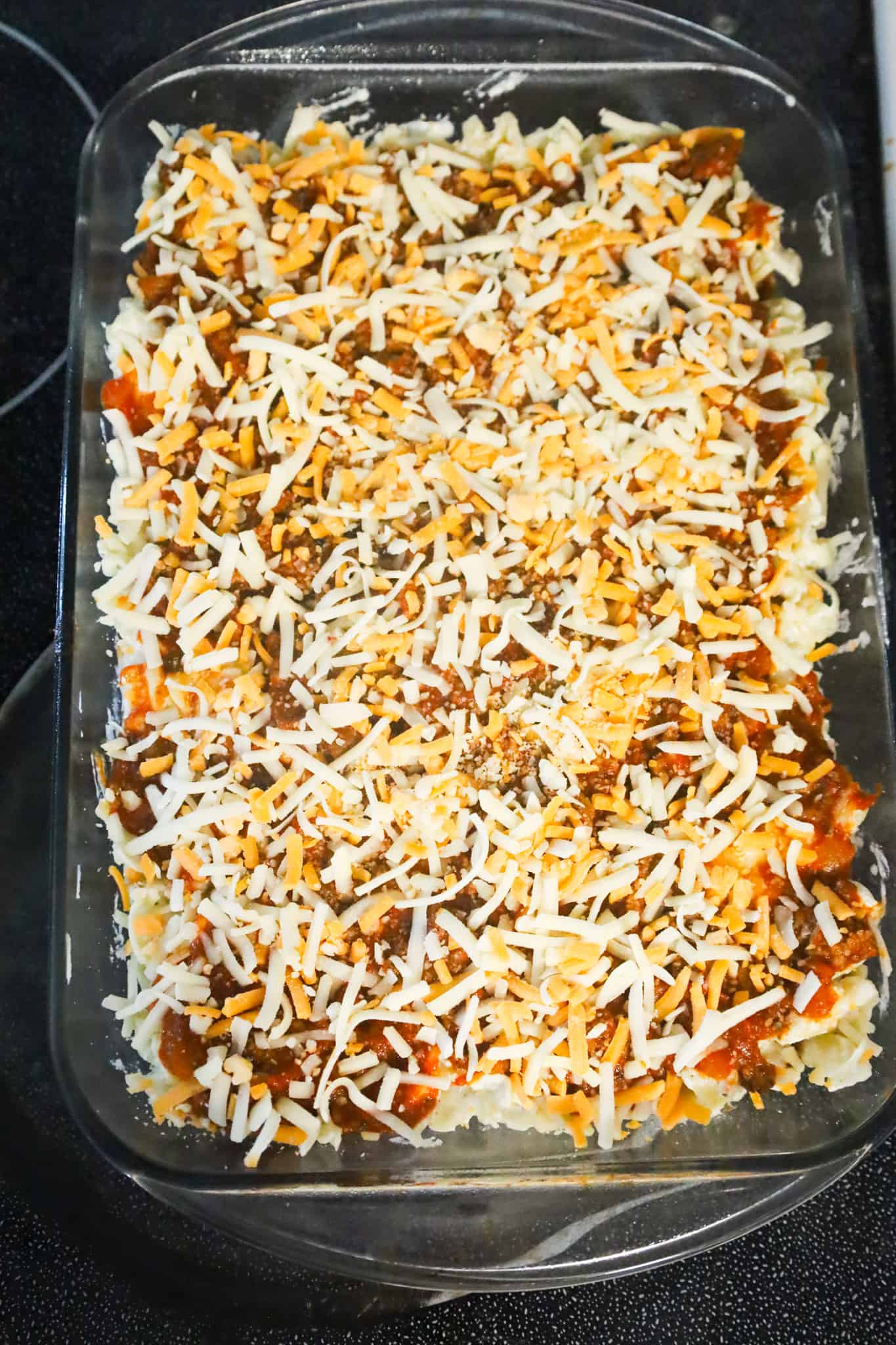 shredded mozzarella and cheddar on top of noodle mixture in a baking dish