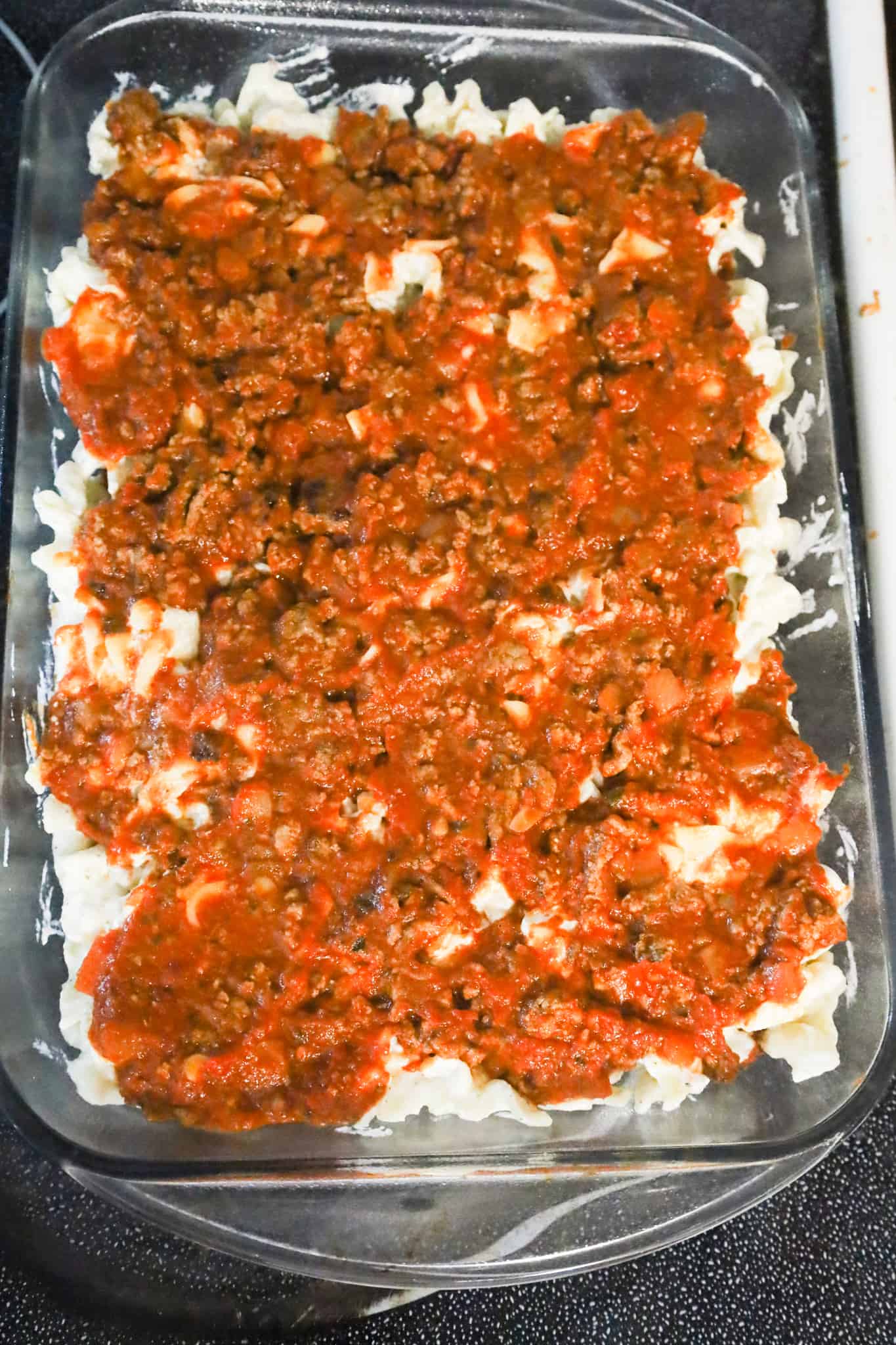 ground beef and marinara mixture on top of noodles in a baking dish