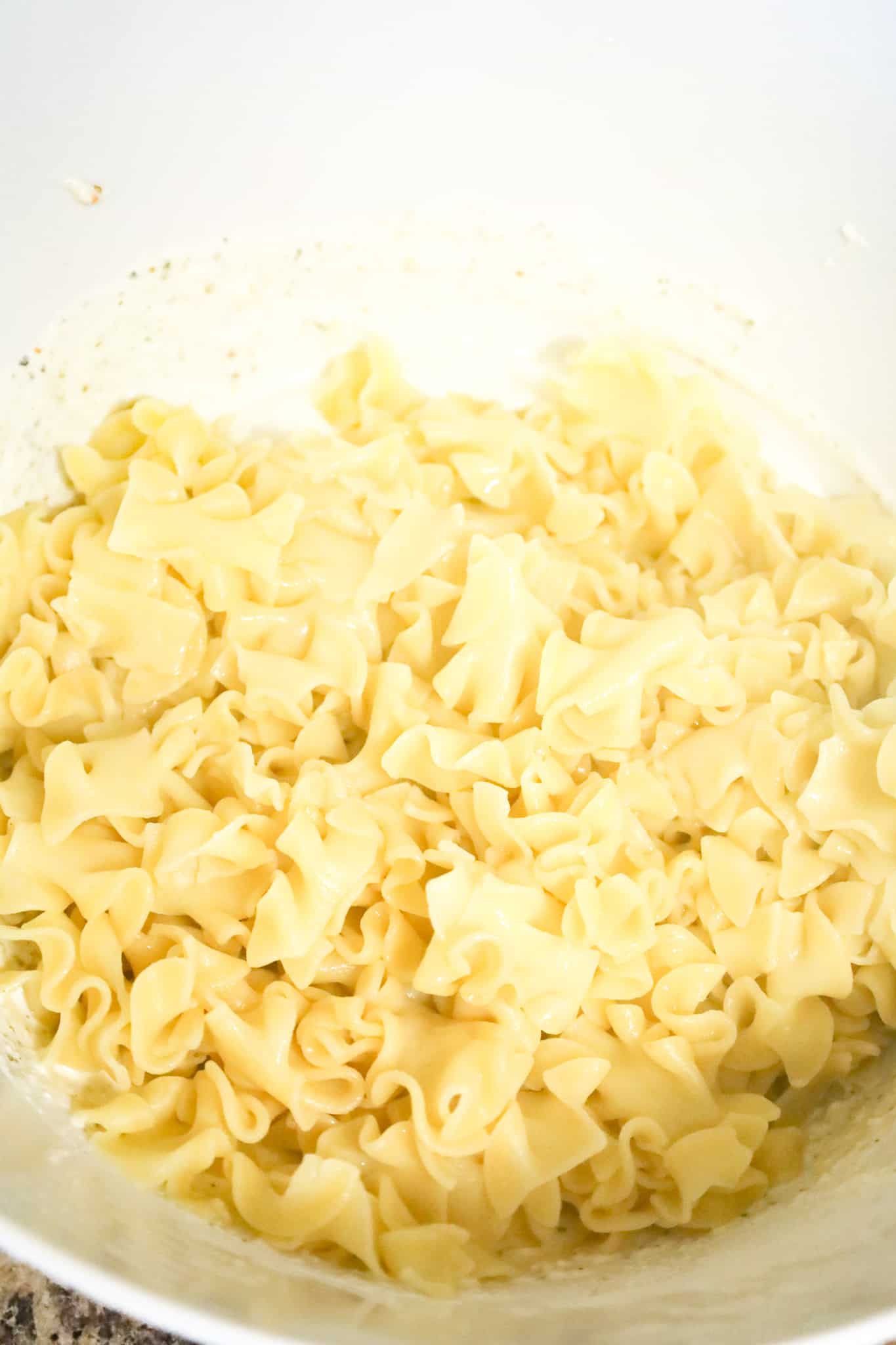 cooked egg noodles in a mixing bowl with ricotta and sour cream mixture in a mixing bowl