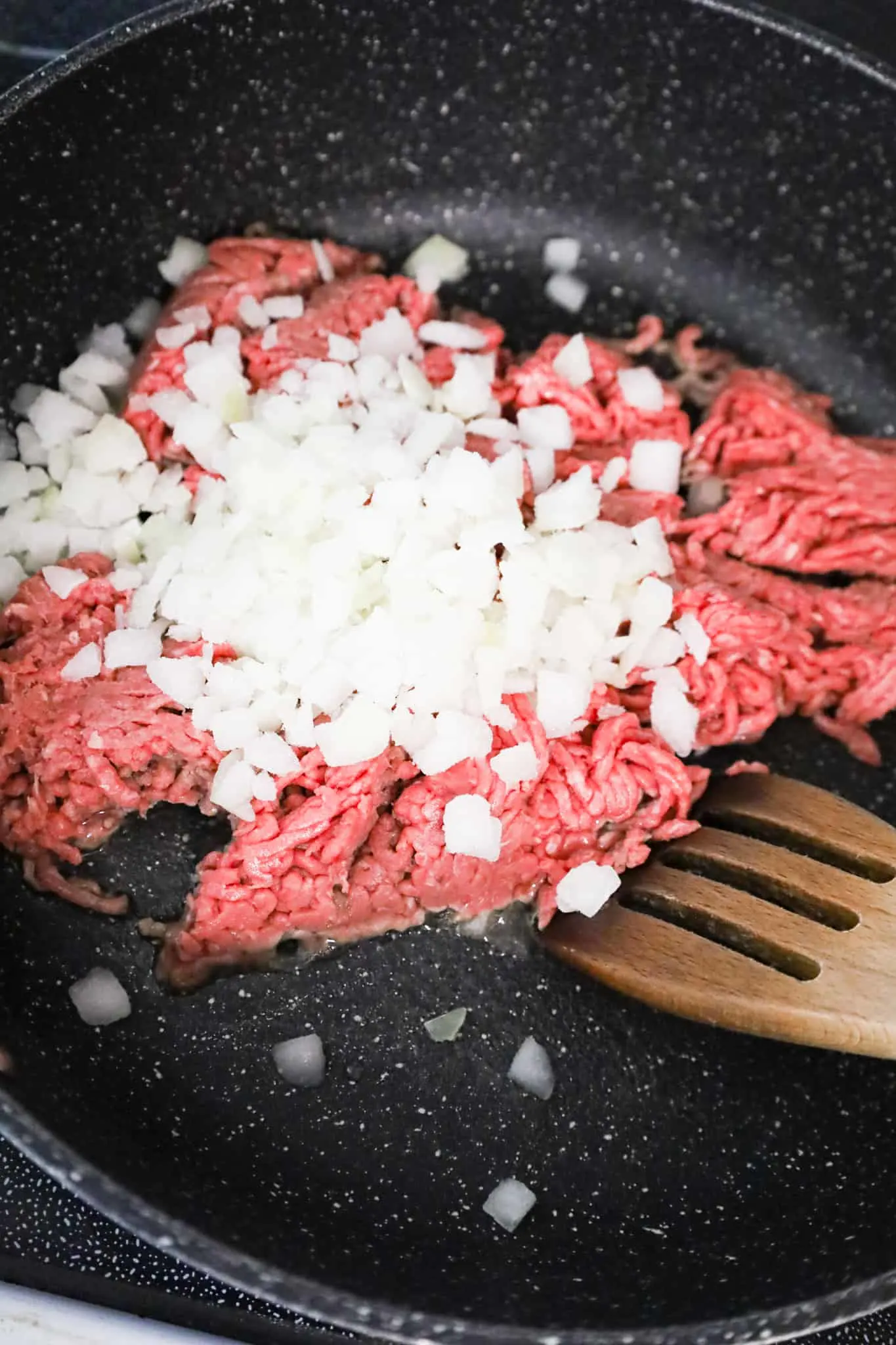 diced onions on top of raw ground beef in a saute pan