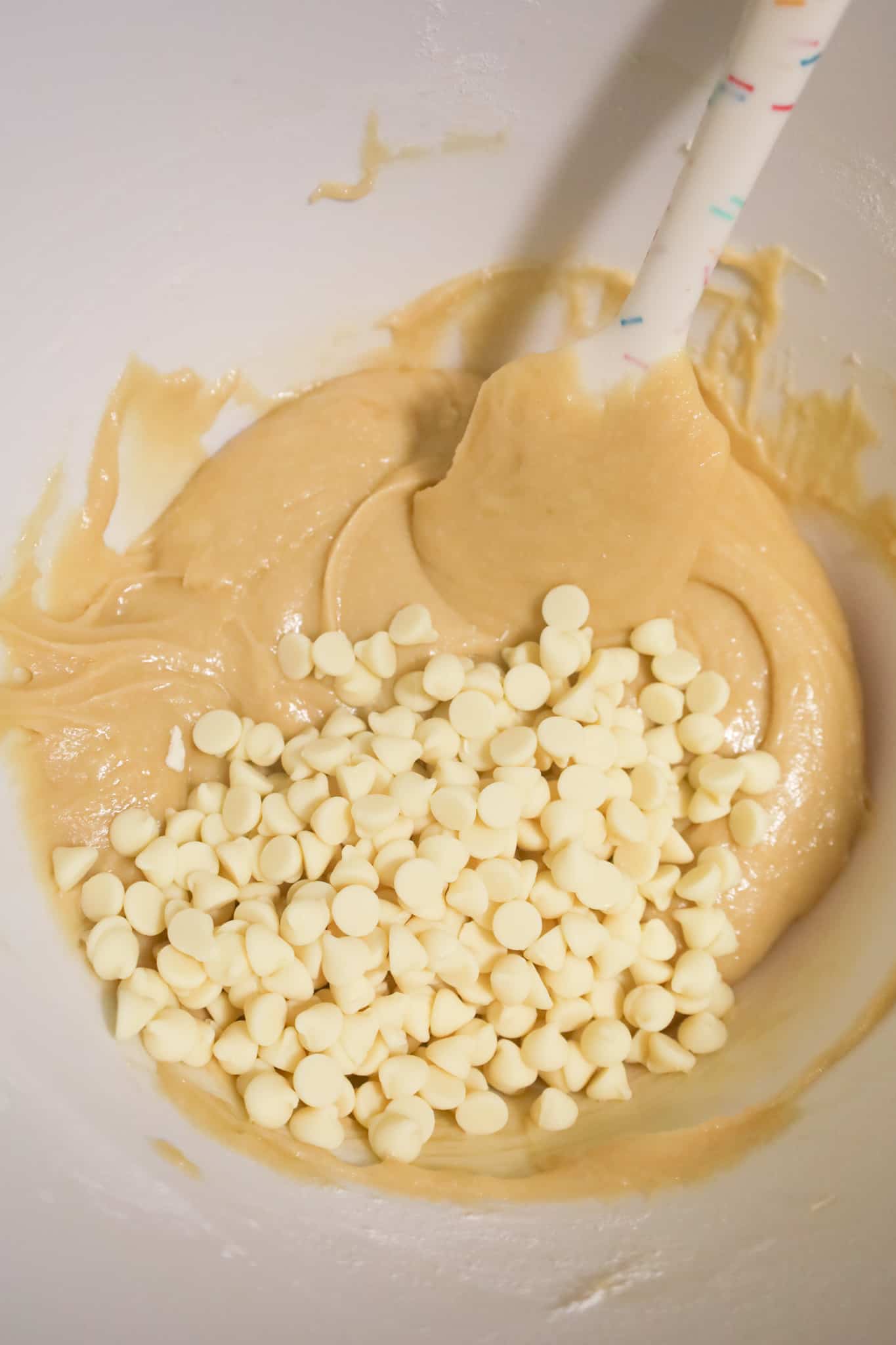 white chocolate chips on top of vanilla brownie batter in a mixing bowl