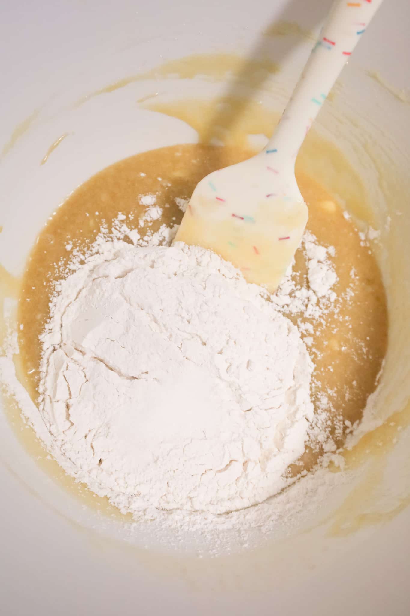 all purpose flour on top of melted butter and sugar mixture in a mixing bowl
