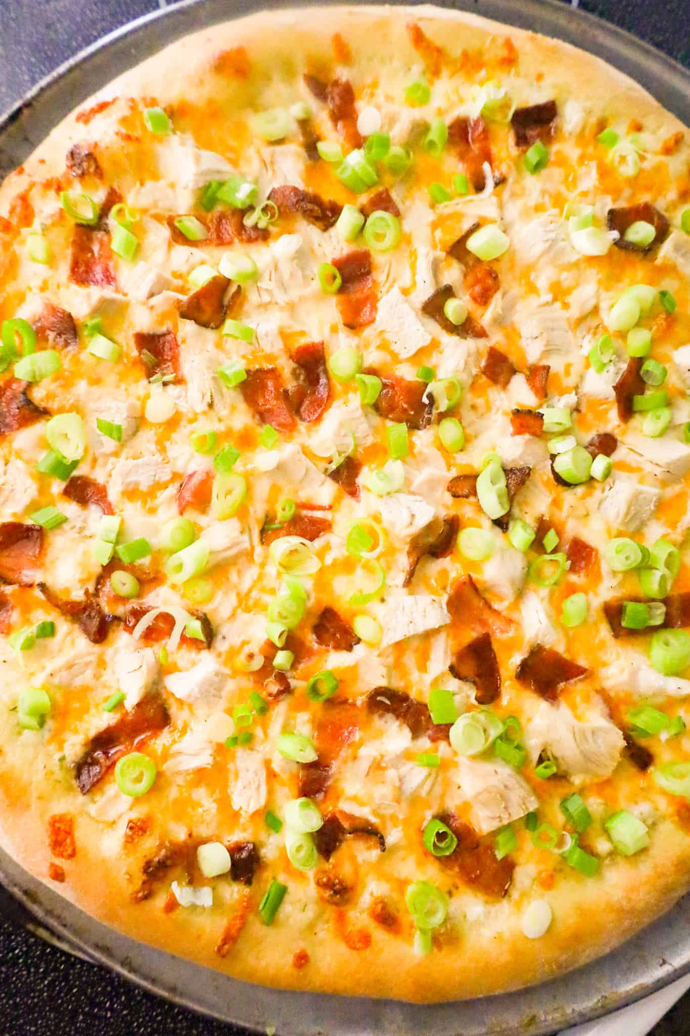 chopped green onions on top of chicken and bacon pizza after baking