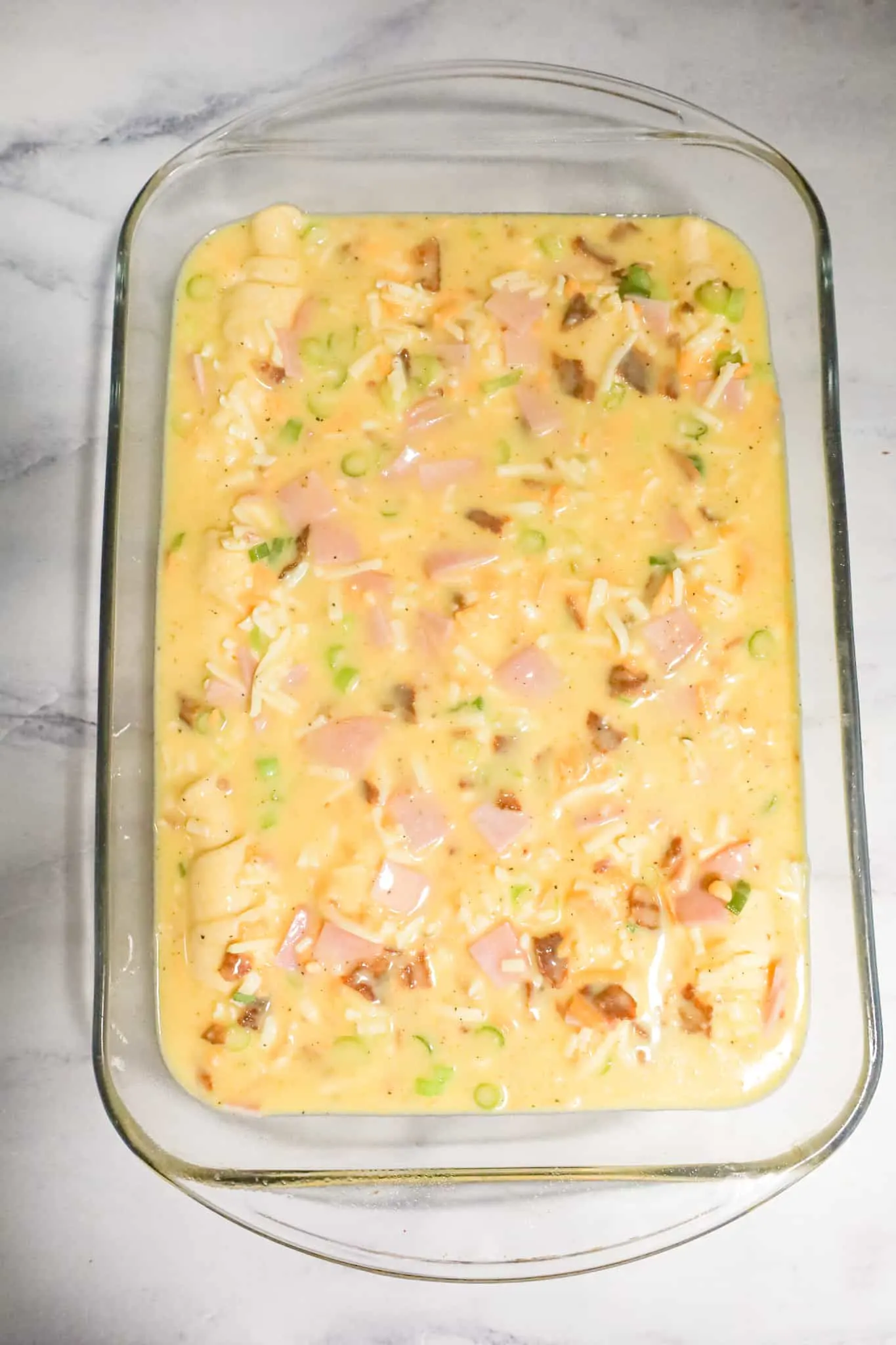 egg mixture with chopped green onions, crumbled bacon and chopped ham poured over crescent dough in a baking dish.
