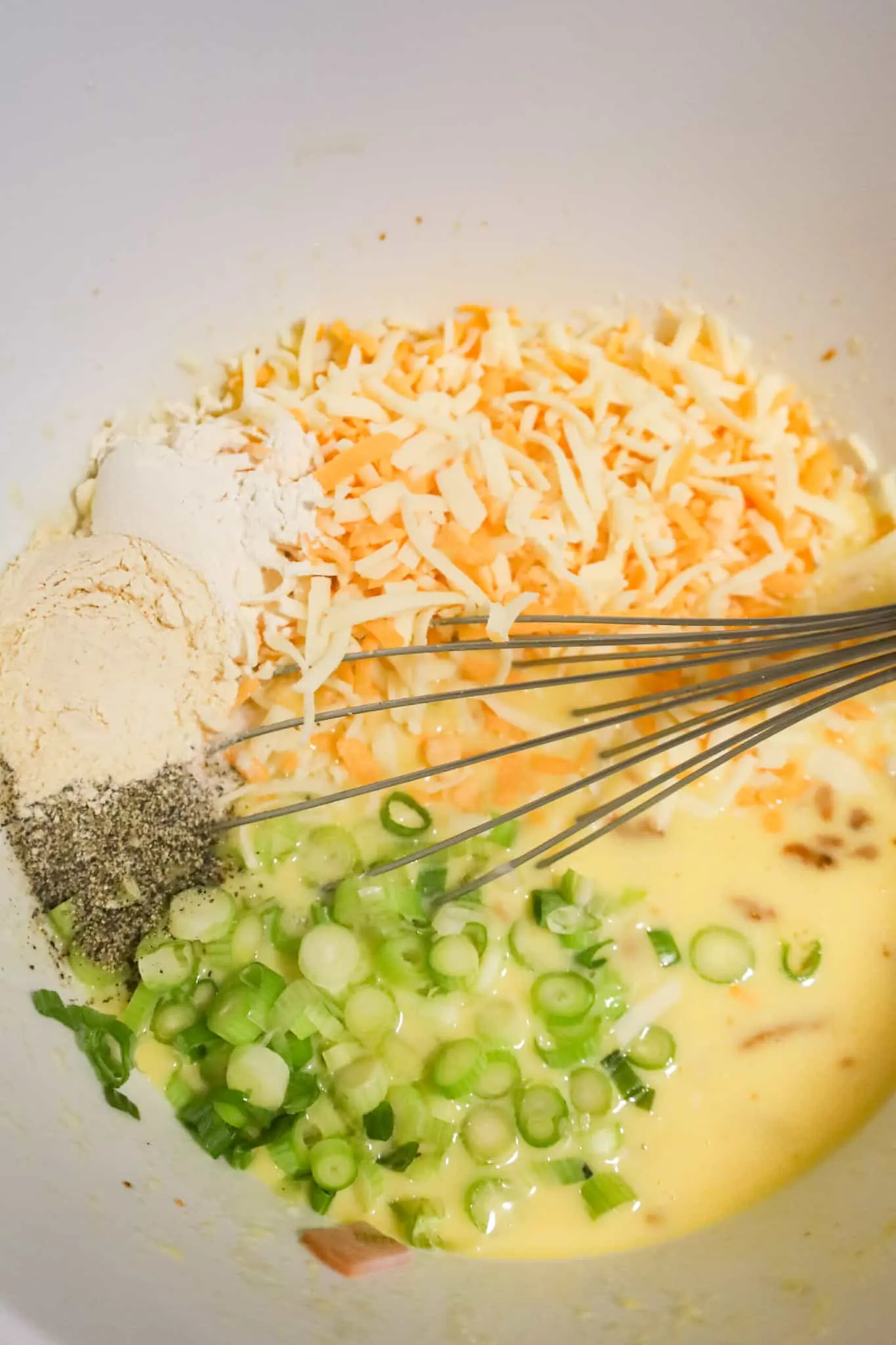 shredded cheese, chopped green onions and spices on top of egg mixture in a mixing bowl