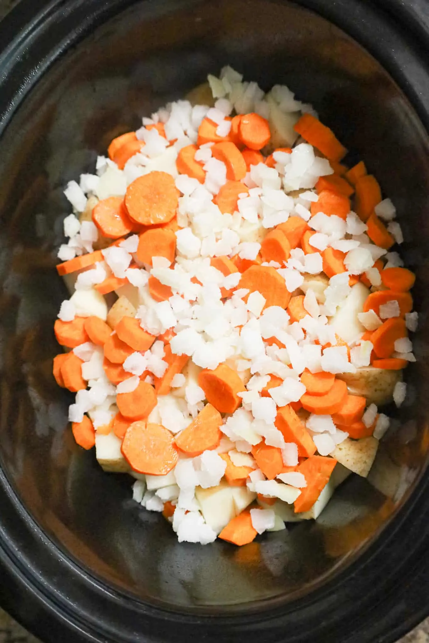 diced onions, sliced carrots and potato chunks in a crock pot