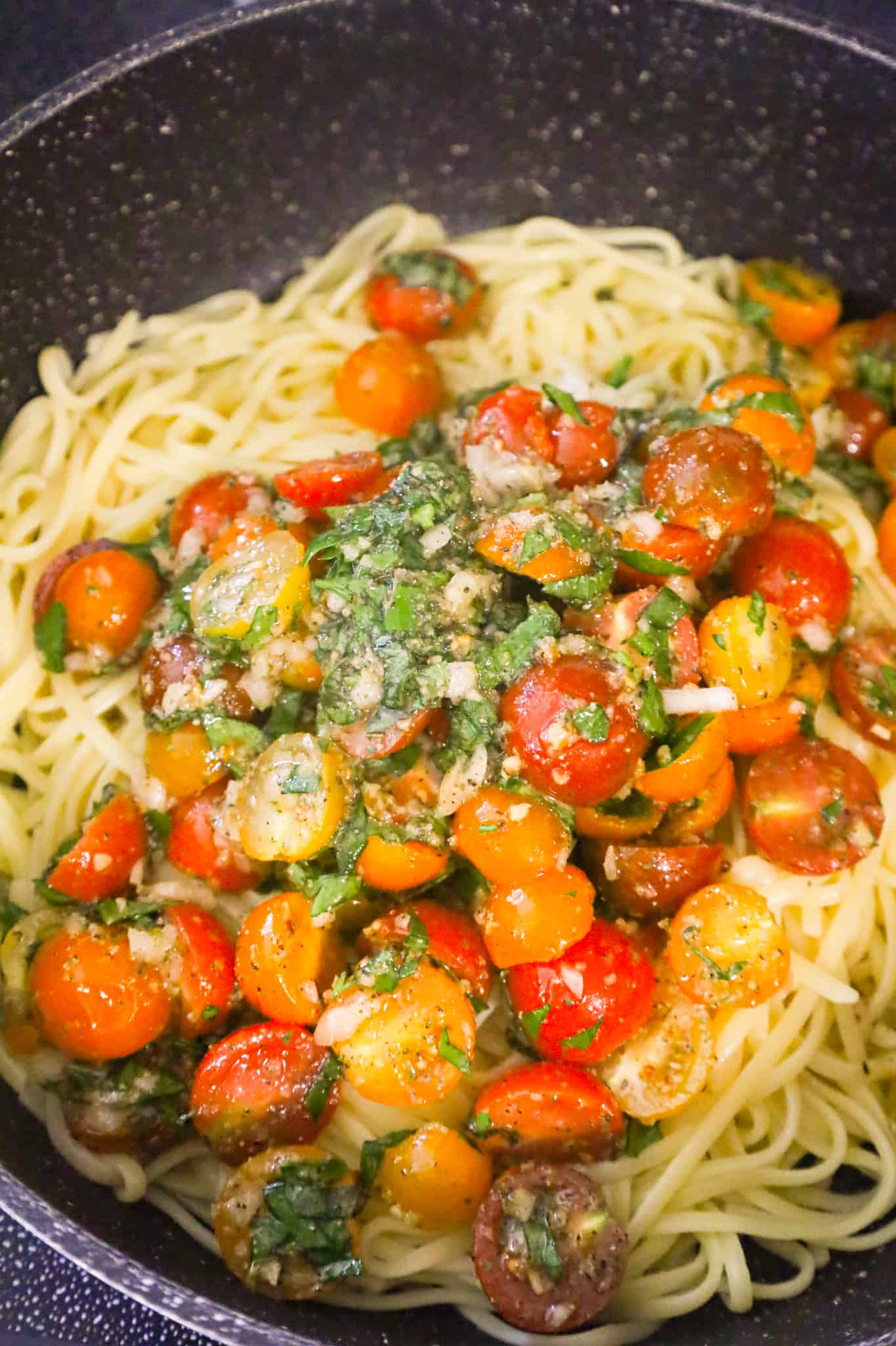 cherry tomato and herb mixture on top of cooked linguine in saute pan