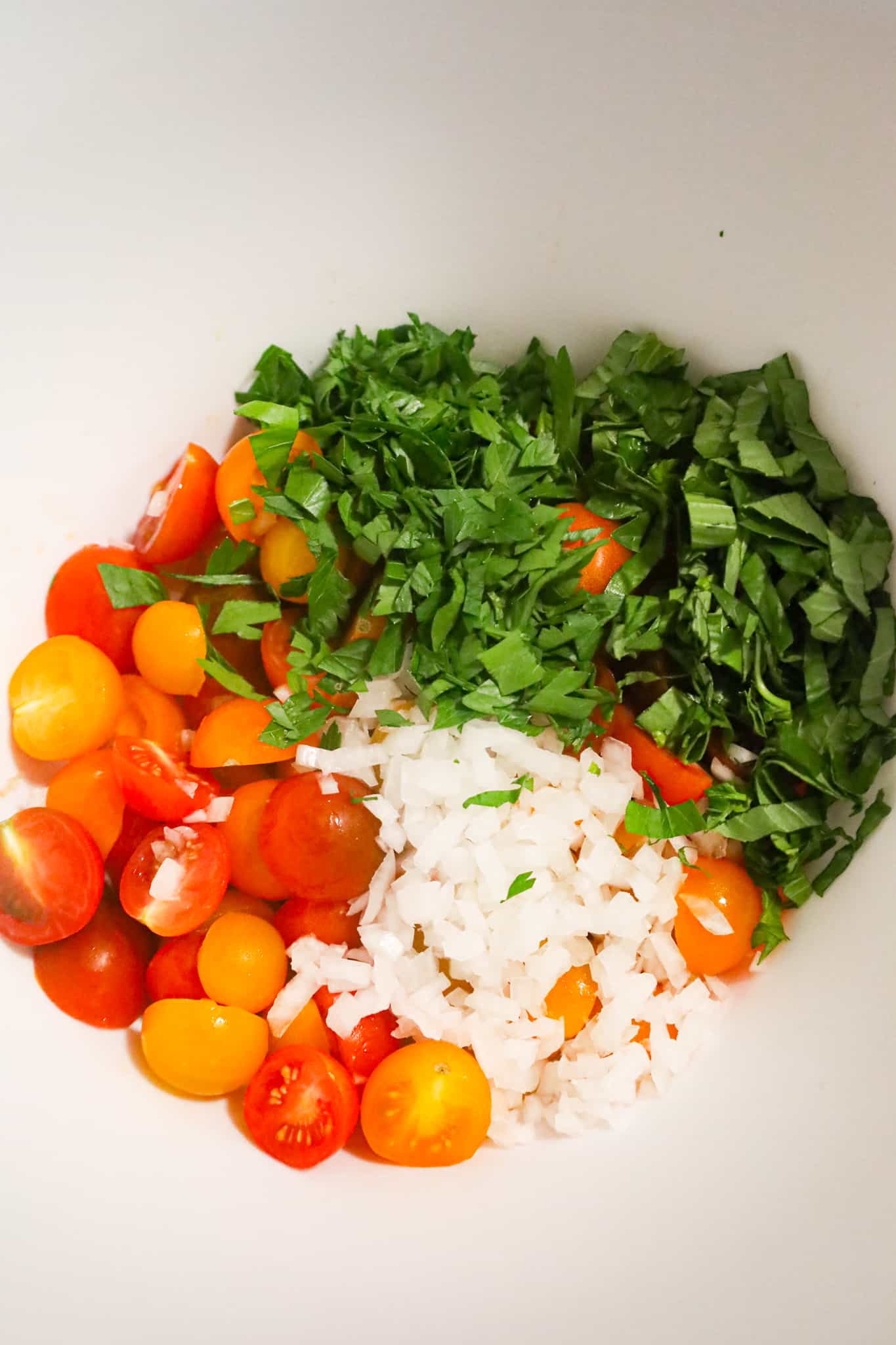 chopped herbs, diced onions and halved cherry tomatoes in a mixing bowl