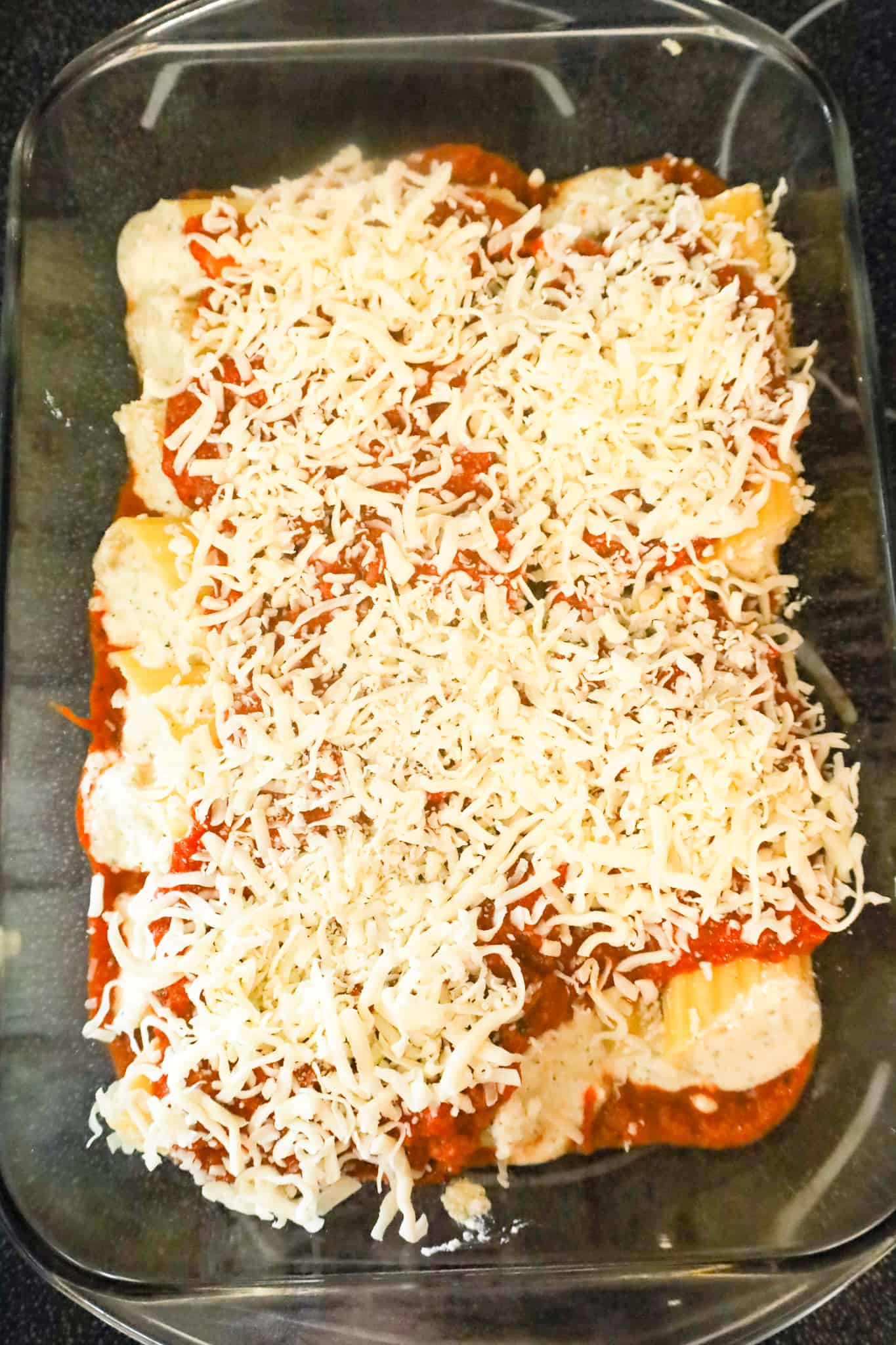 shredded mozzarella on top of manicotti in a baking dish