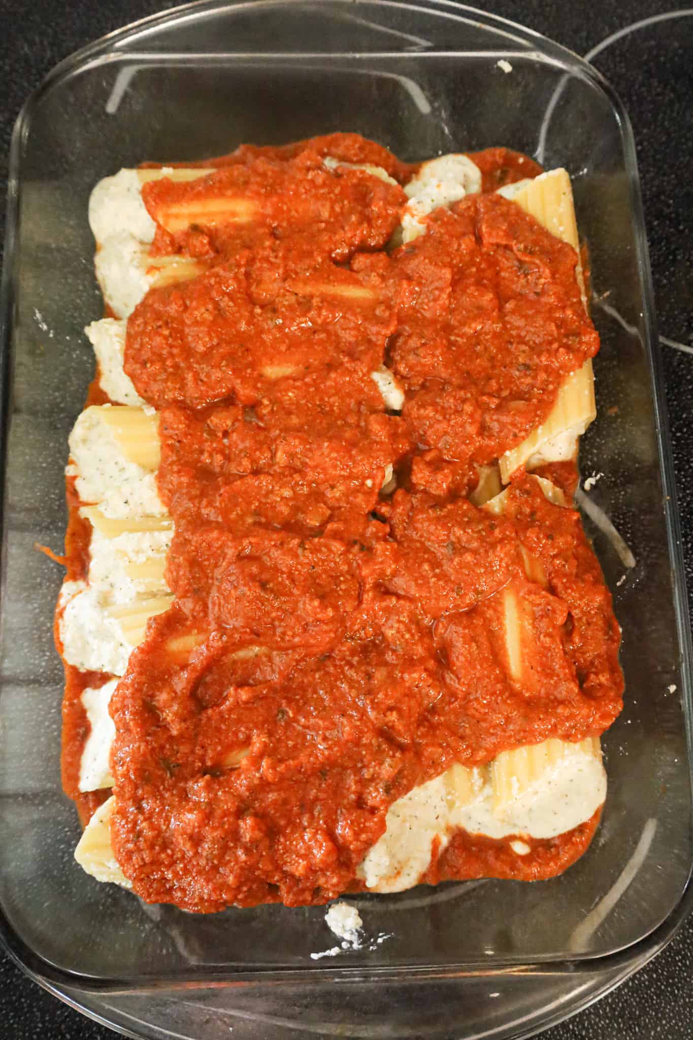 bolognese sauce on top of ricotta stuffed manicotta in a baking dish